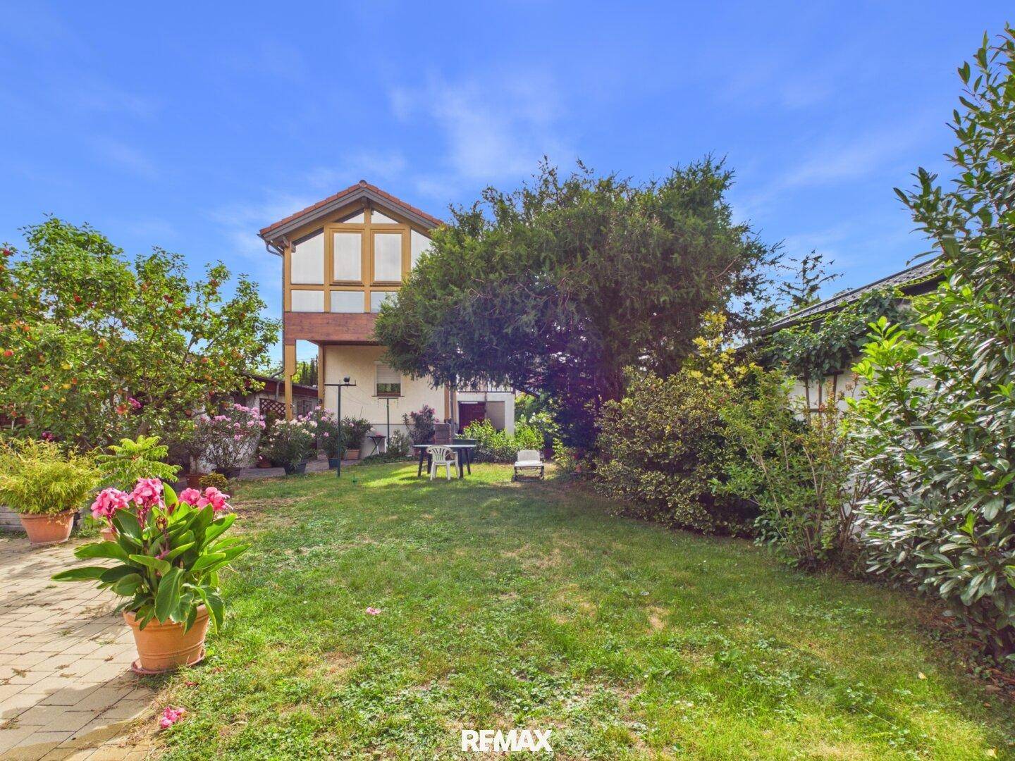 Gepflegter Garten mit Rasen, üppiger Bepflanzung und einem Haus im Hintergrund an einem sonnigen Tag.