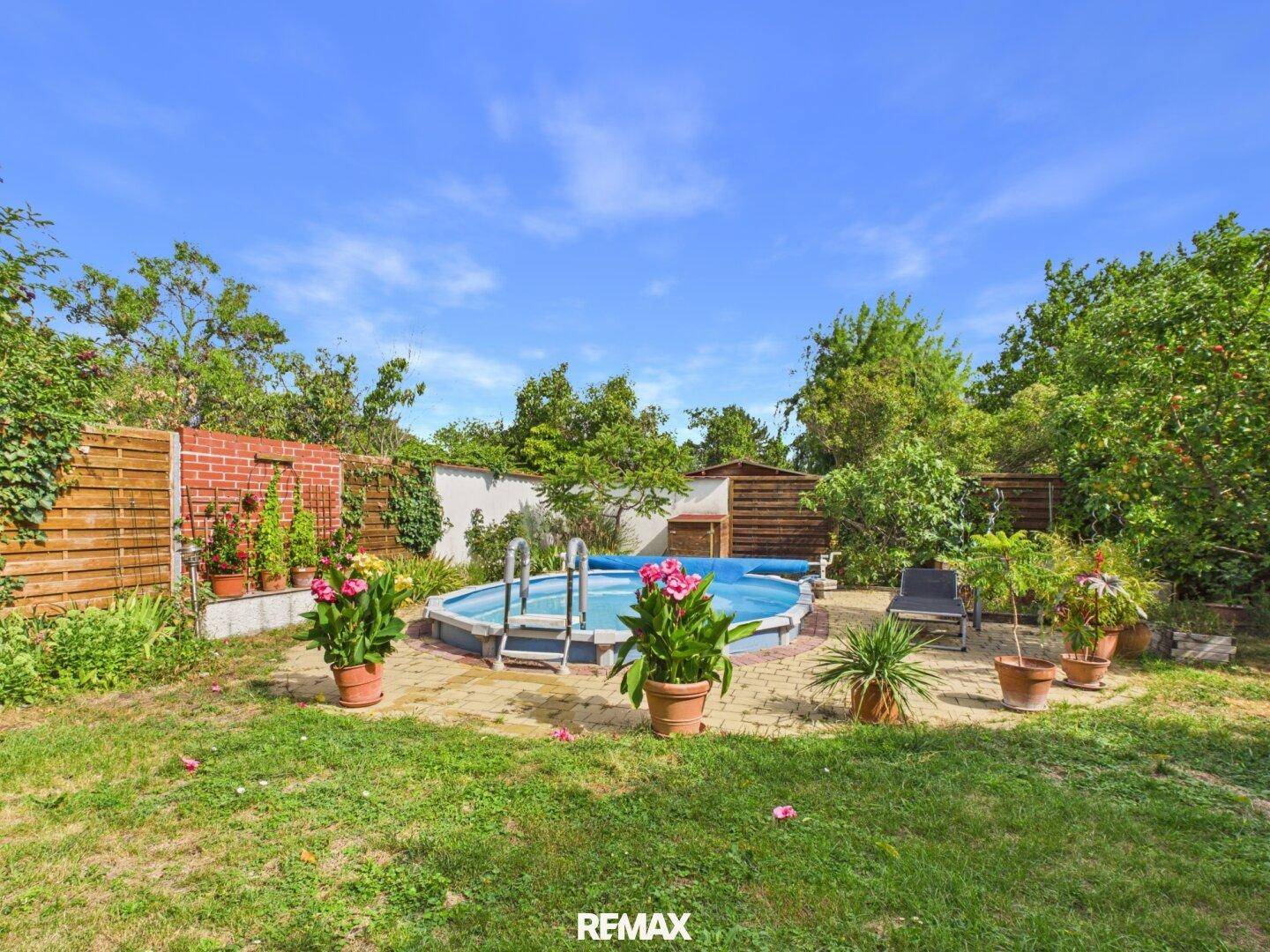 Gartenansicht mit Aufstellpool, gepflastertem Bereich und einem kleinen Gartenhaus im Hintergrund.