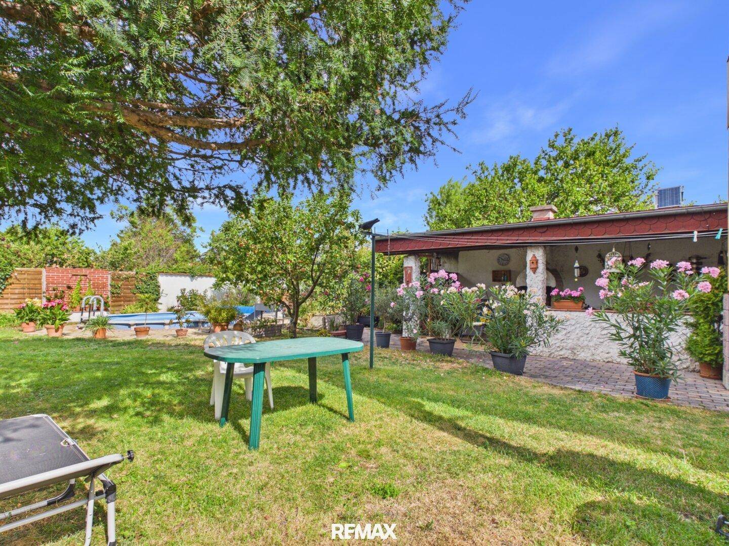 Sonniger Garten mit Rasenfläche und Blick auf die überdachte Terrasse mit Außenkamin.