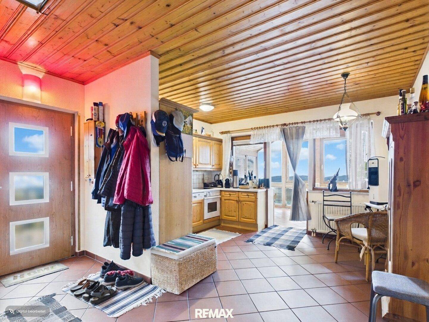 Heller Eingangsbereich mit Holzdecke, Fliesenboden und einer kleinen integrierten Küchenzeile.