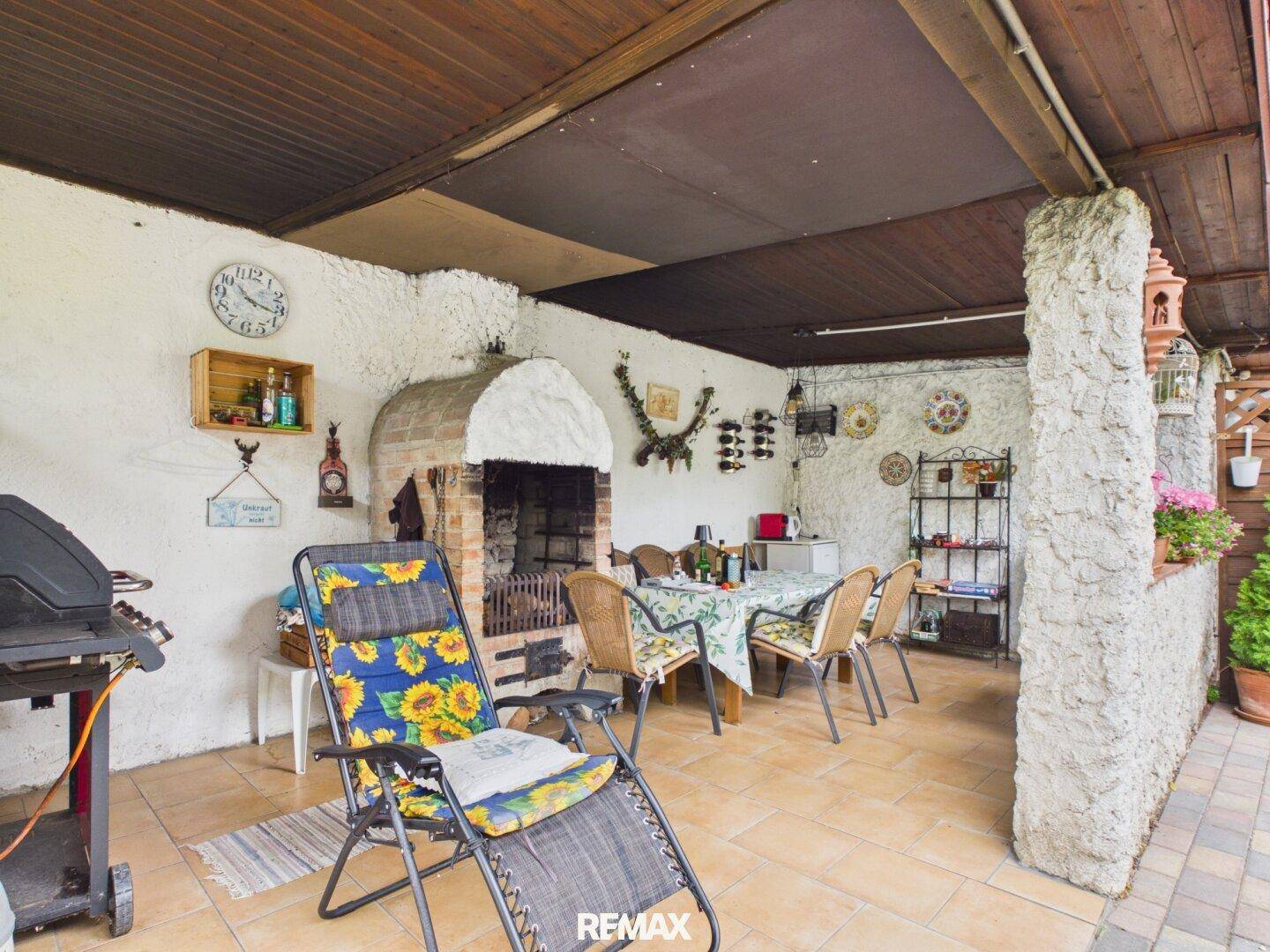 Überdachte Terrasse mit rustikalem Außenkamin, Essbereich und Liegestuhl für entspannte Stunden.