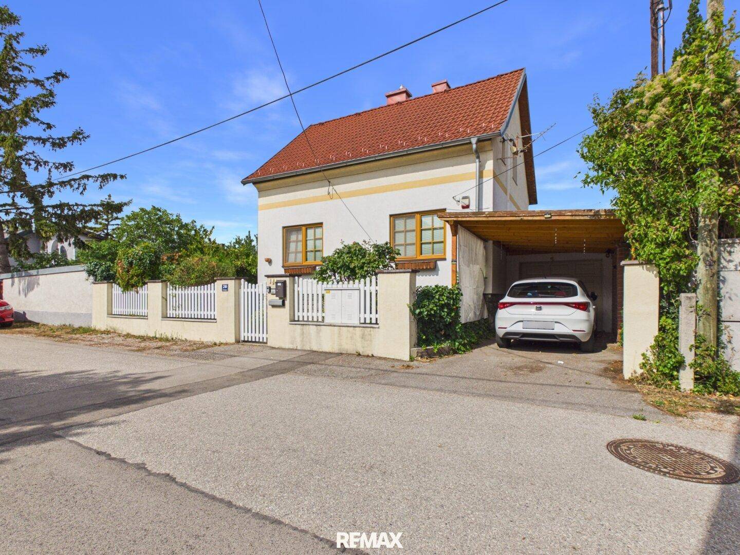 Charmantes Einfamilienhaus mit Satteldach, weißem Zaun und Carport an einer ruhigen Straße.