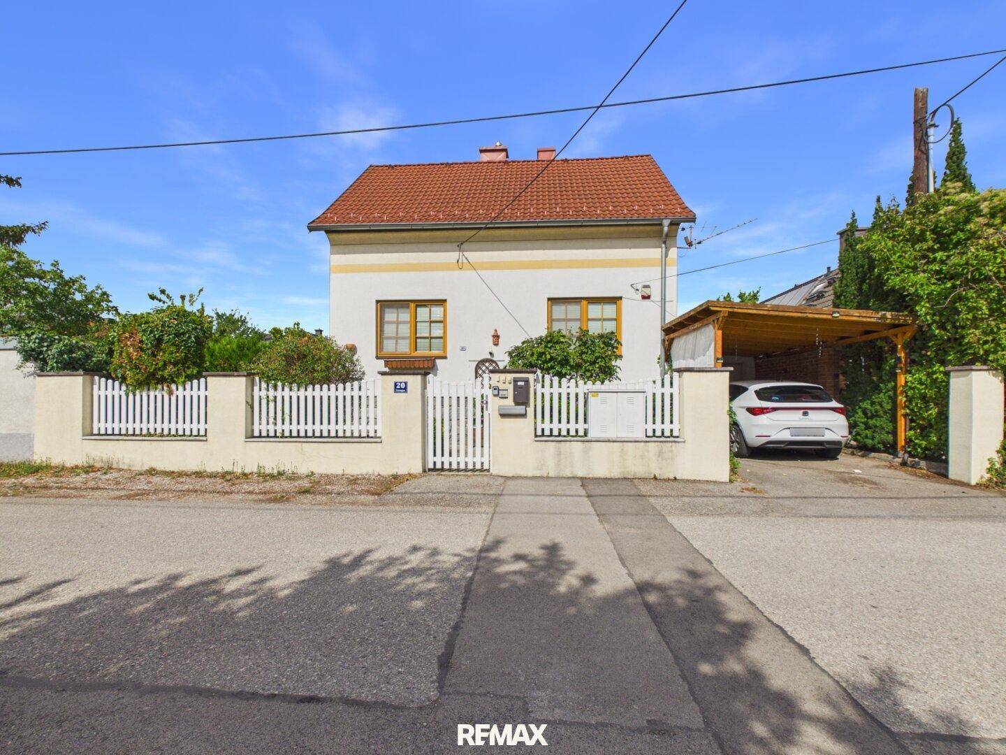 Gepflegtes Einfamilienhaus mit Carport und weißem Lattenzaun an einem sonnigen Tag.