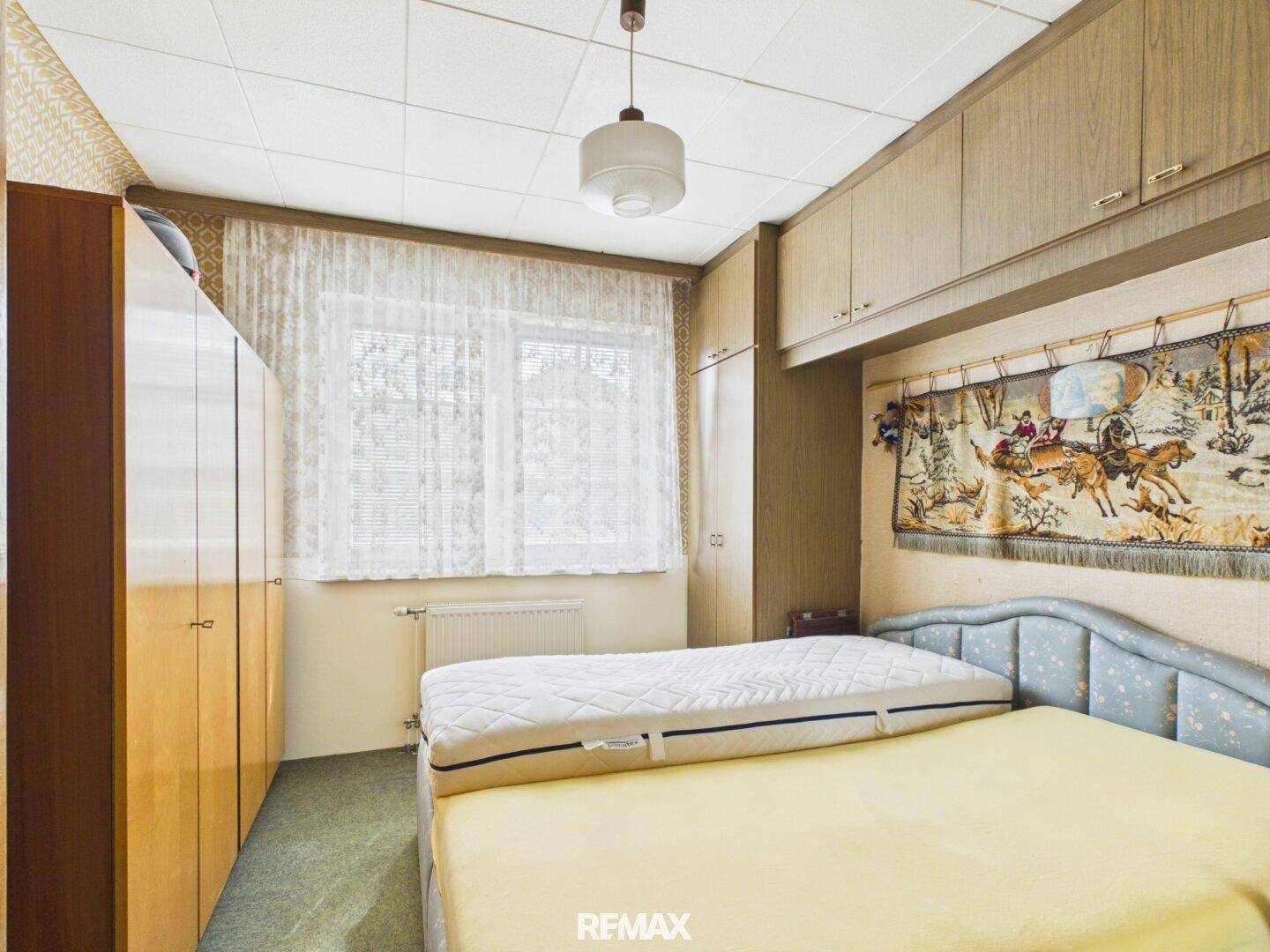 Schlafzimmer mit Doppelbett, integrierten Schränken und einem Fenster mit Vorhängen, das für natürliches Licht sorgt.