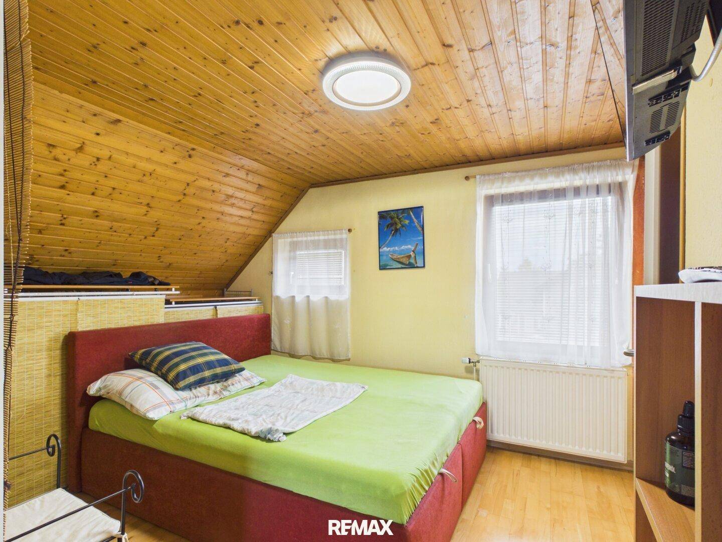 Gemütliches Schlafzimmer mit Holzdecke, Holzboden und schrägen Wänden im Dachgeschoss.