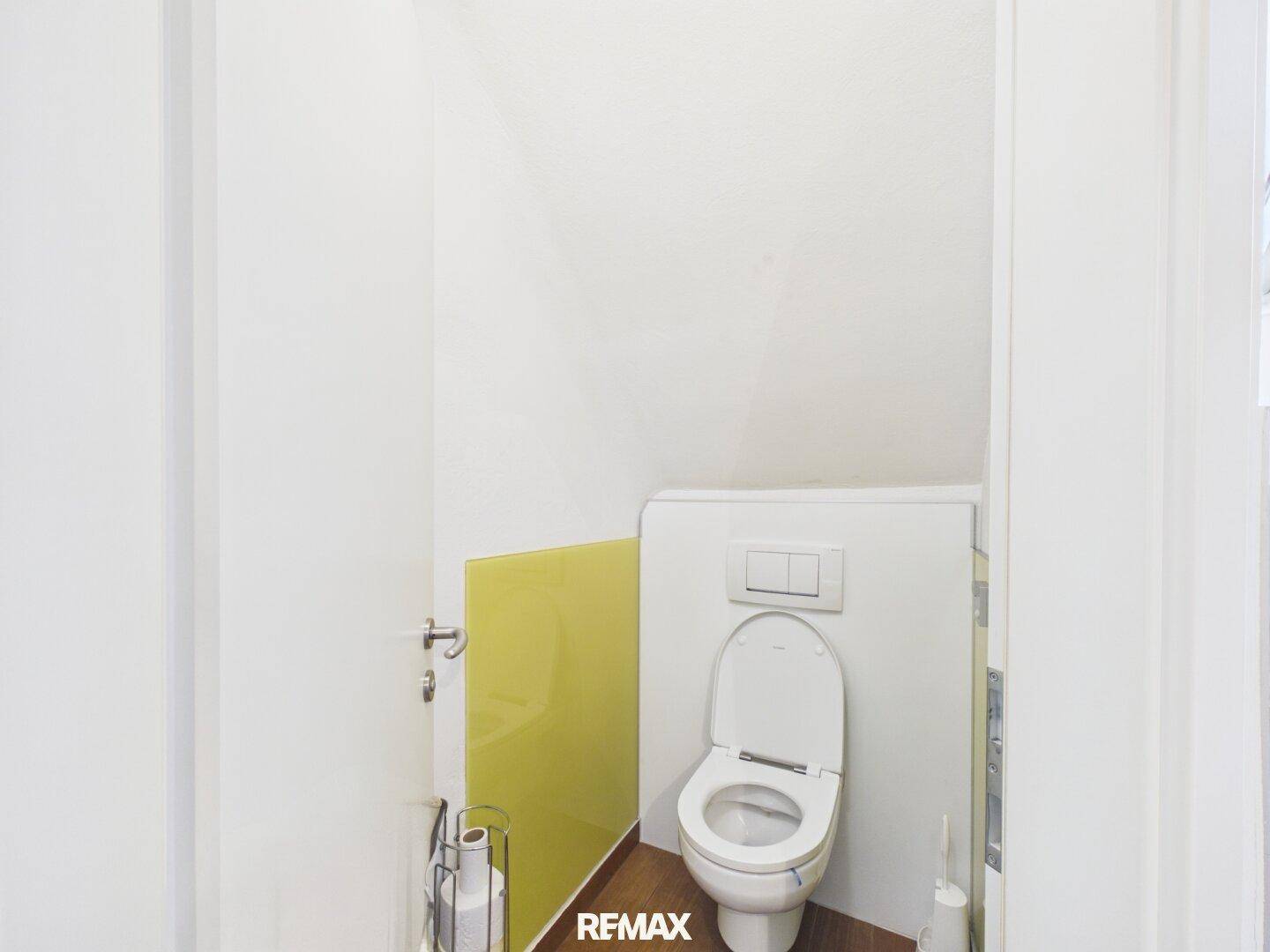 Separates WC mit weißer Toilette und schrägen Wänden im Dachgeschoss.