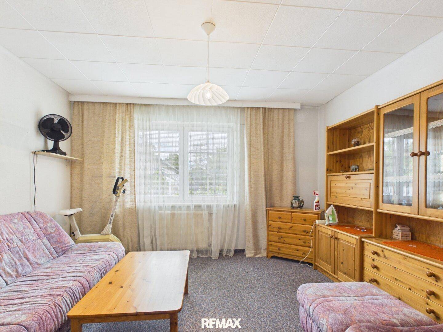 Gemütliches Wohnzimmer mit Sofa, Holztisch und Schrankwand, gut beleuchtet durch ein großes Fenster.