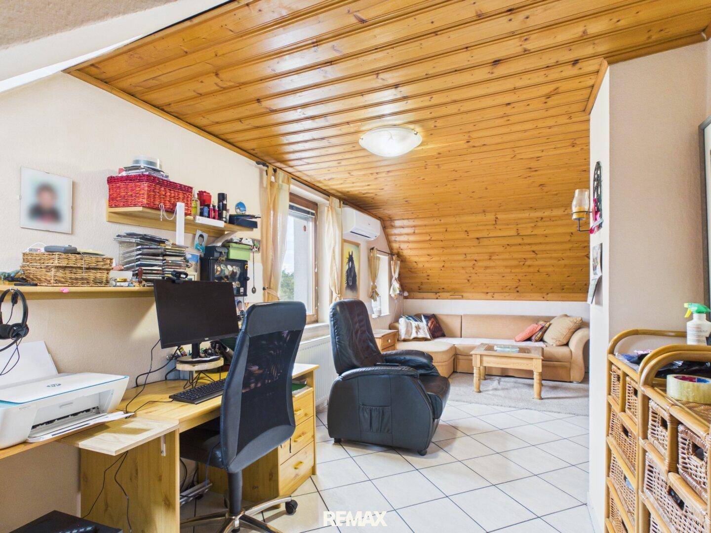 Vielseitiger Raum im Dachgeschoss mit Arbeitsbereich, Sofa und Holzdeckenverkleidung.