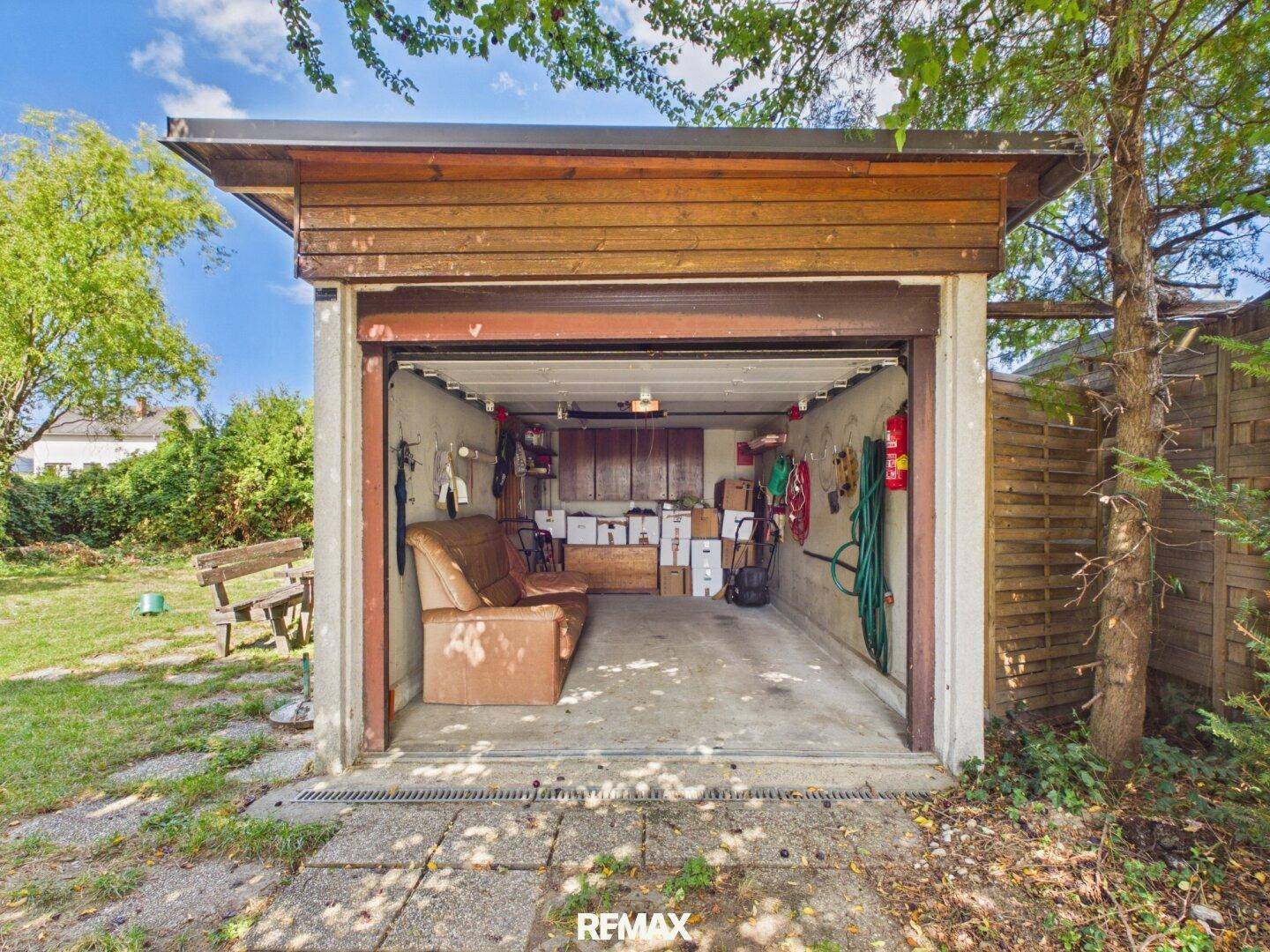 Offene Garage mit Holzelementen, genutzt als Abstellraum und mit einer Couch ausgestattet.