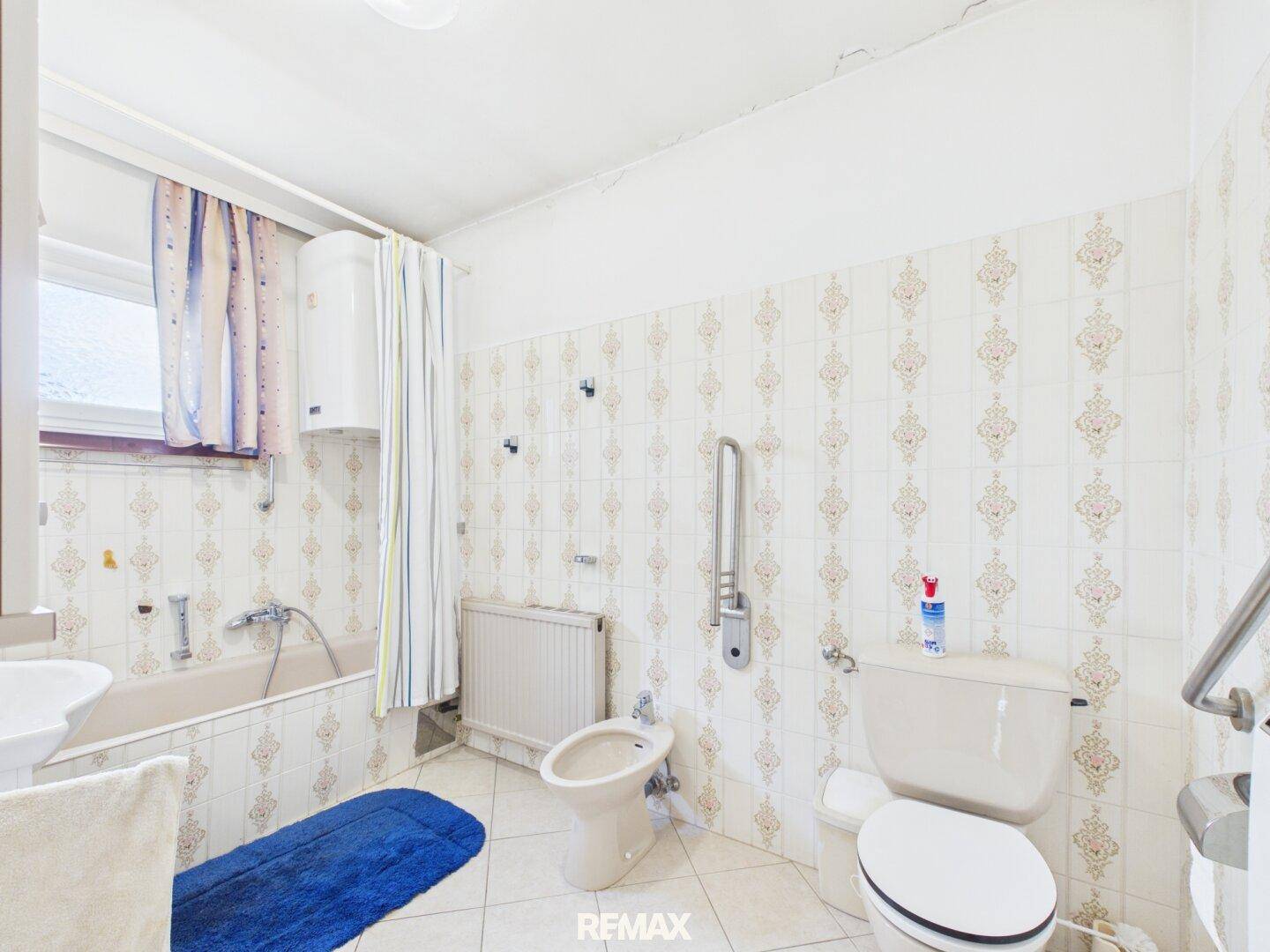 Badezimmer mit Toilette, Badewanne und Haltegriffen für mehr Sicherheit.