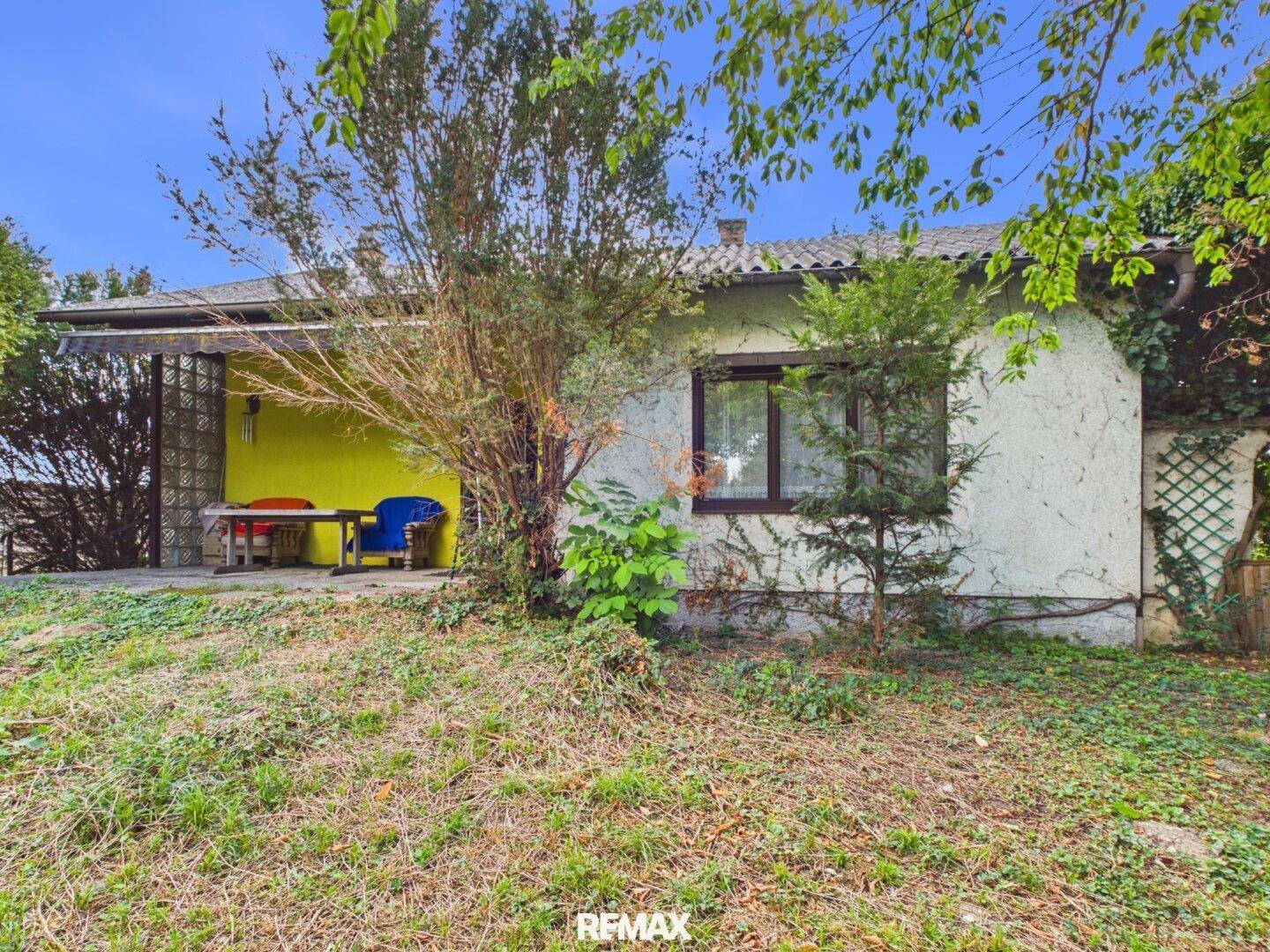 Rückansicht des Hauses mit überdachter Terrasse und umgebender Vegetation.