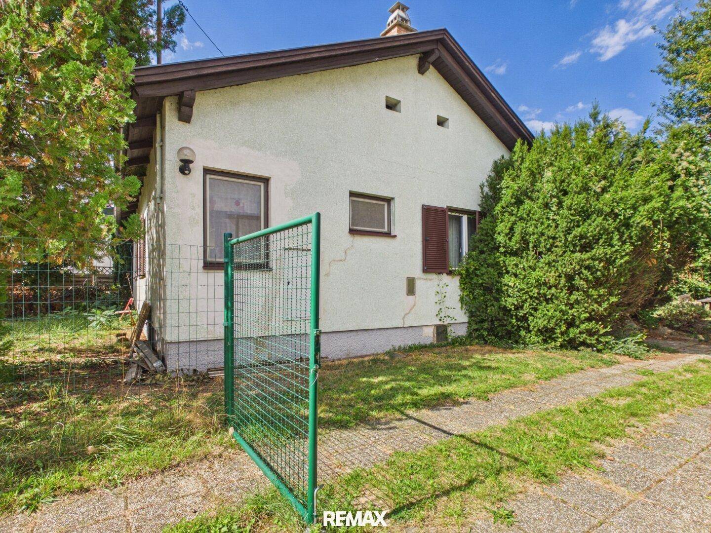 Seitenansicht des Hauses mit grünem Gartentor und gepflasterter Zufahrt.