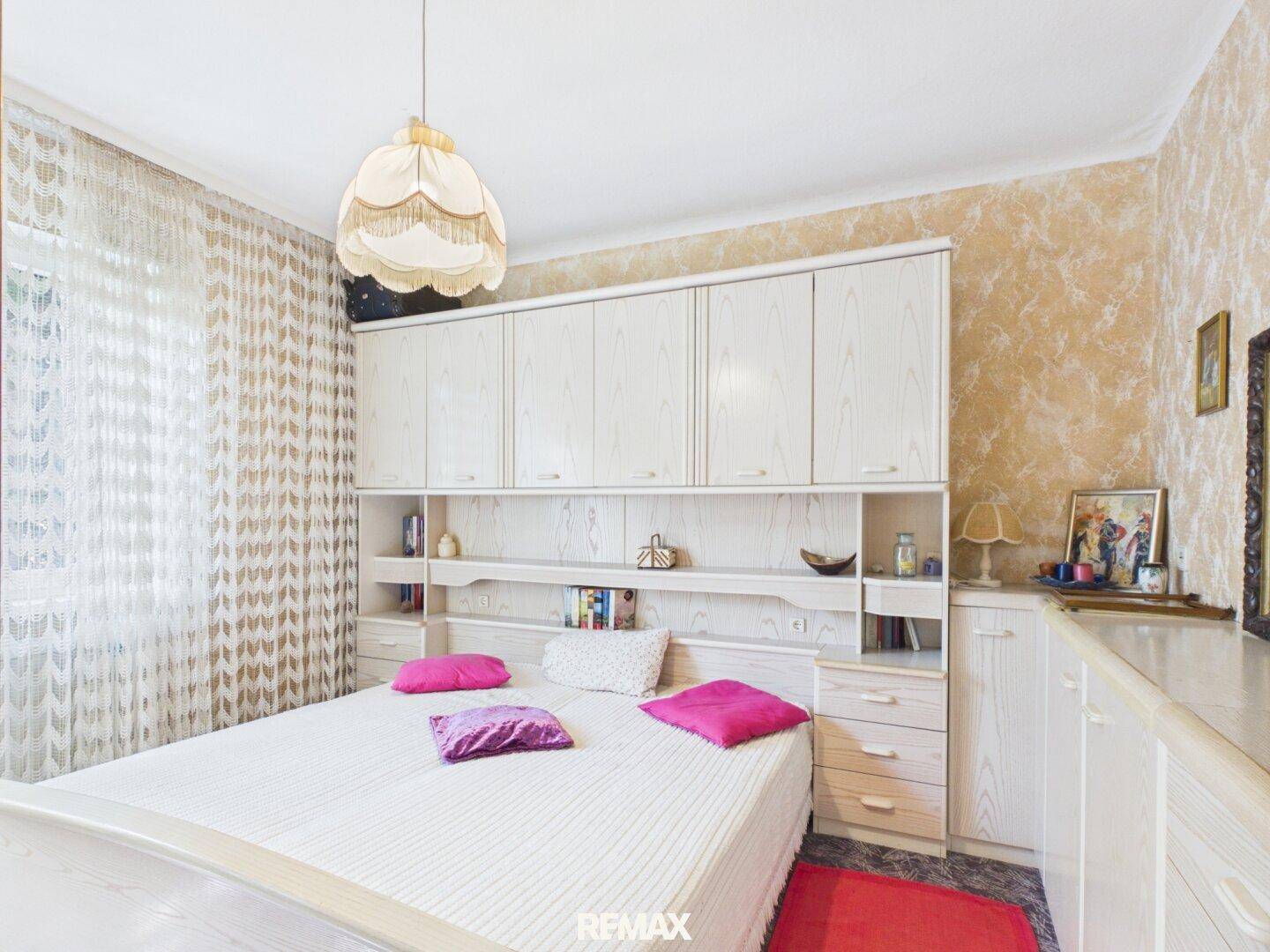 Schlafzimmer mit großem Bett, Einbauschränken und gemusterter Tapete.