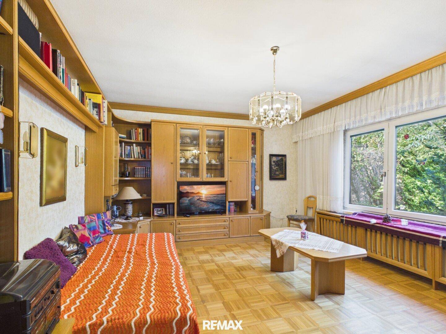 Wohnzimmer mit großem Fenster, Blick ins Grüne und umfangreichen Bücherregalen.