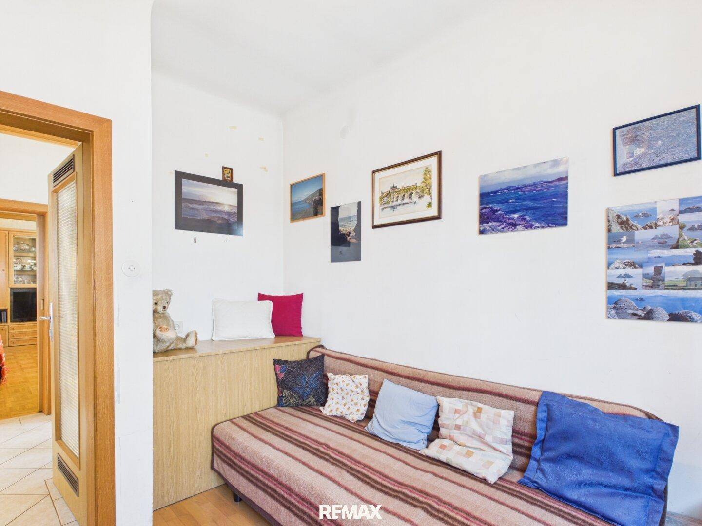 Gästezimmer mit Sofa, Holzelementen und verschiedenen Wanddekorationen.