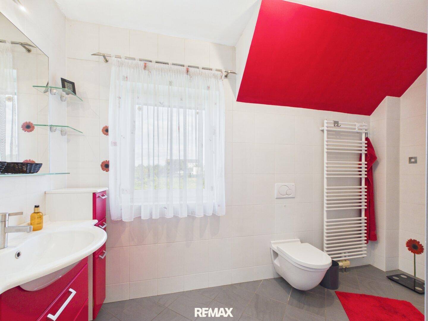 Modernes Badezimmer mit roten Akzenten, wandhängendem WC, Waschbecken und Fenster.
