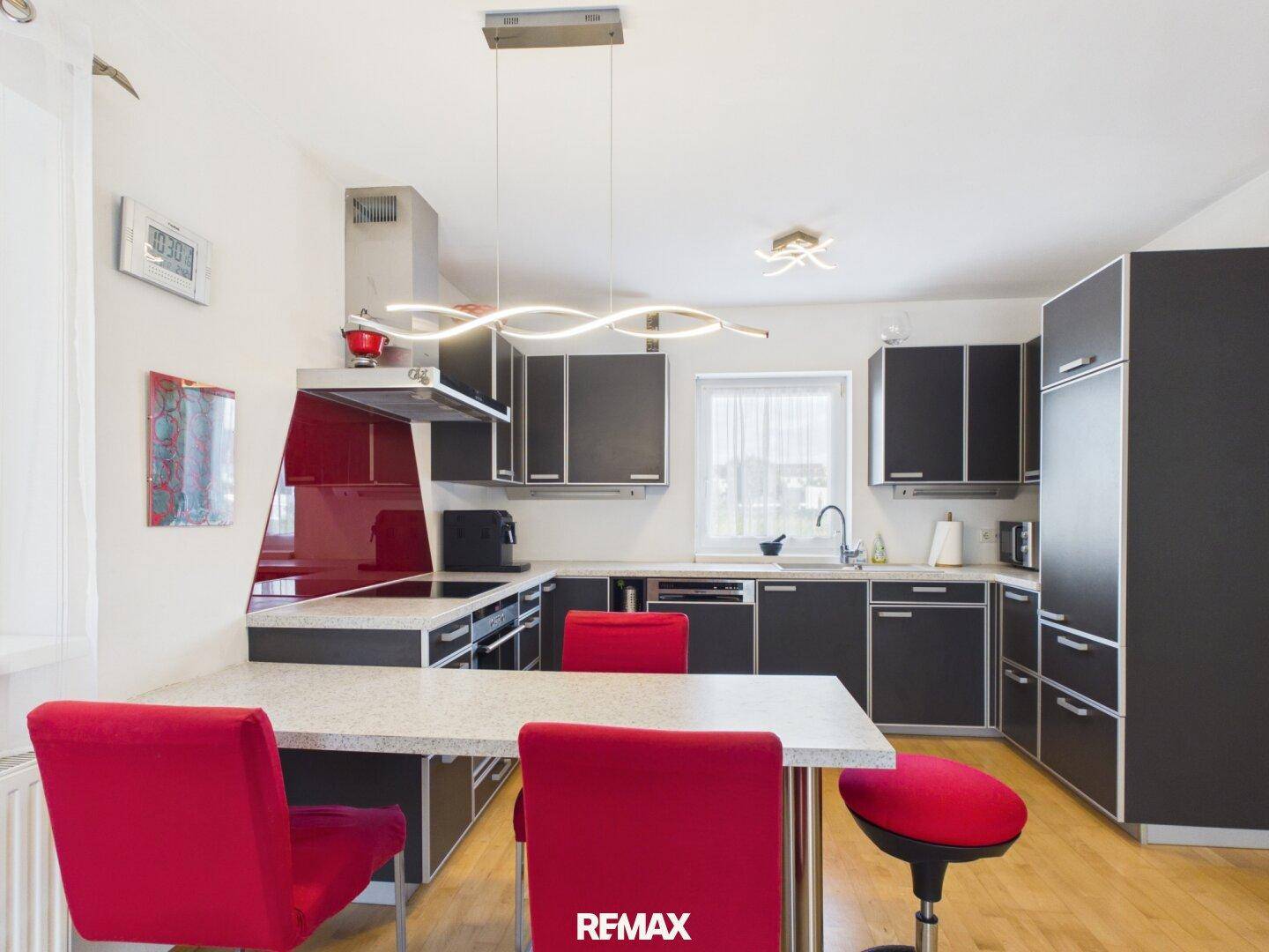 Moderne Einbauküche mit schwarzen Schränken, roter Rückwand und integriertem Essbereich.