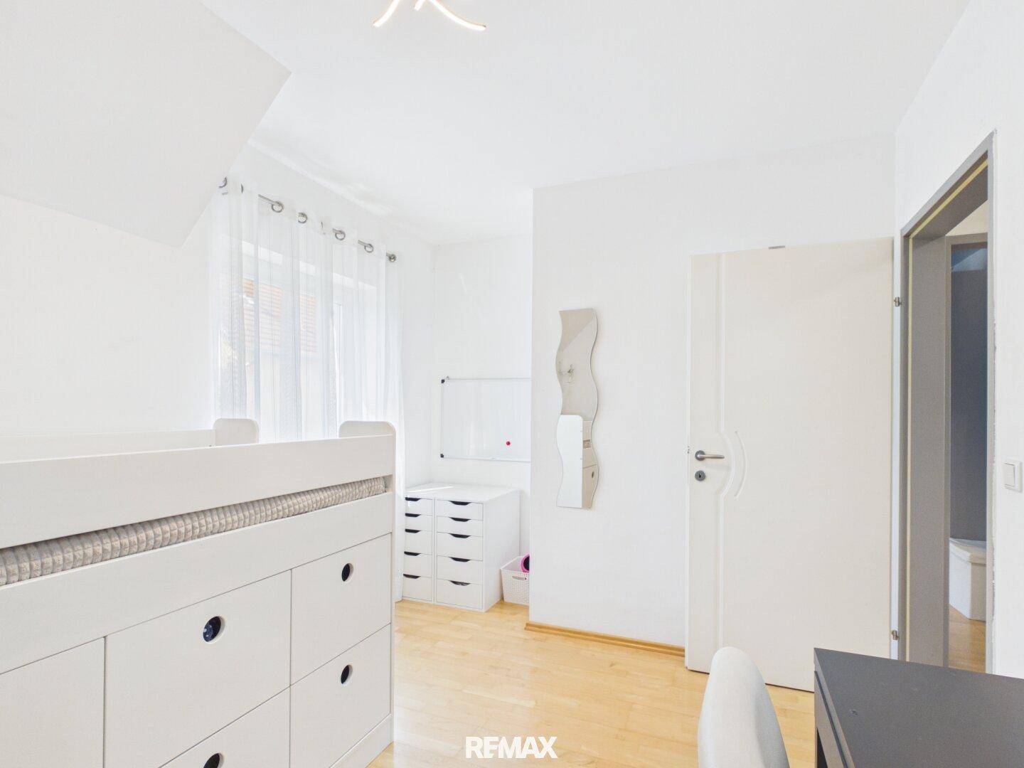 Helles Kinderzimmer mit Holzboden, Fenster und weißem Mobiliar, freundlich und funktional.