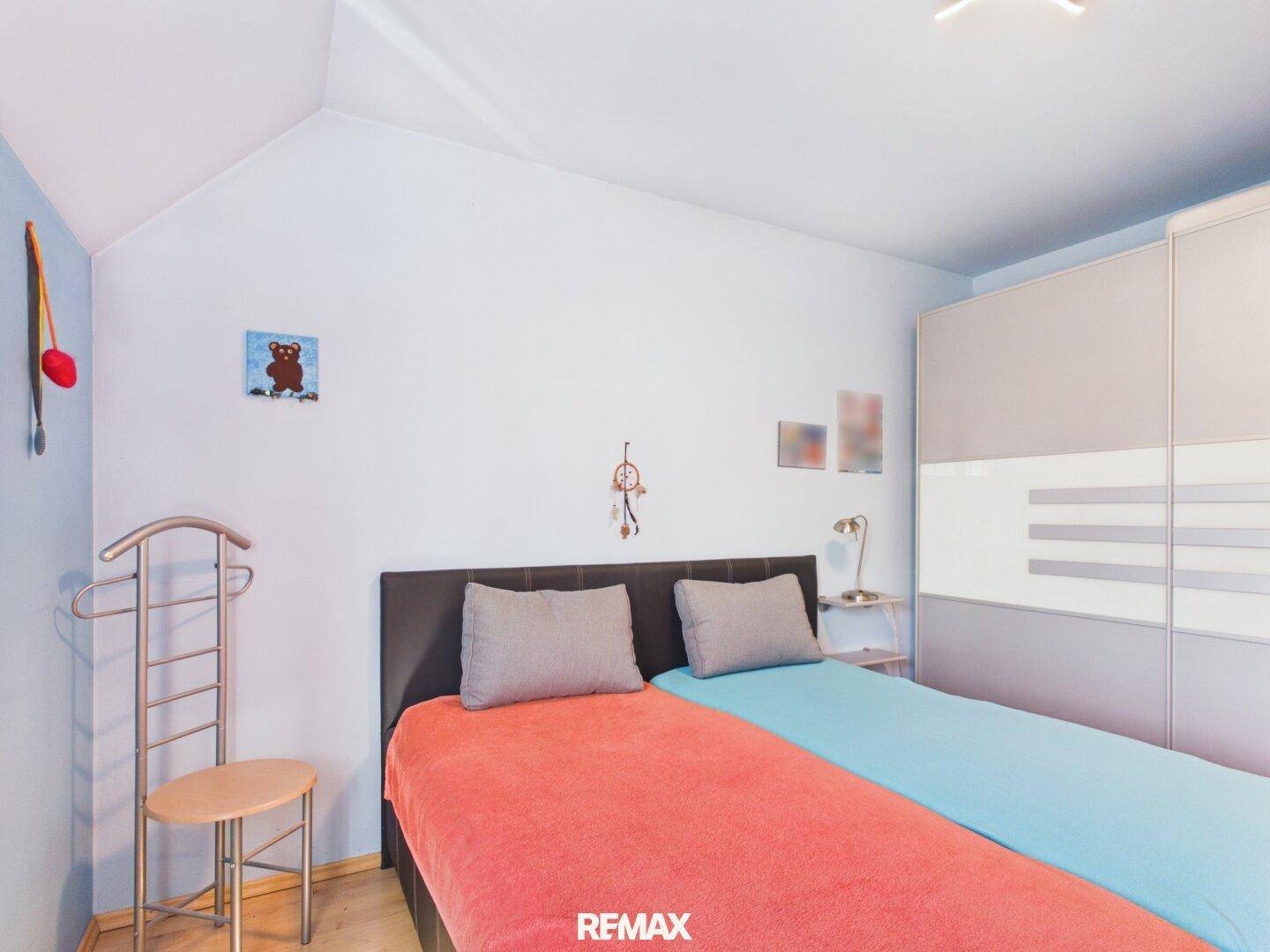 Schlafzimmer mit blauen Wänden, Holzboden und großem Kleiderschrank, hell und geräumig.