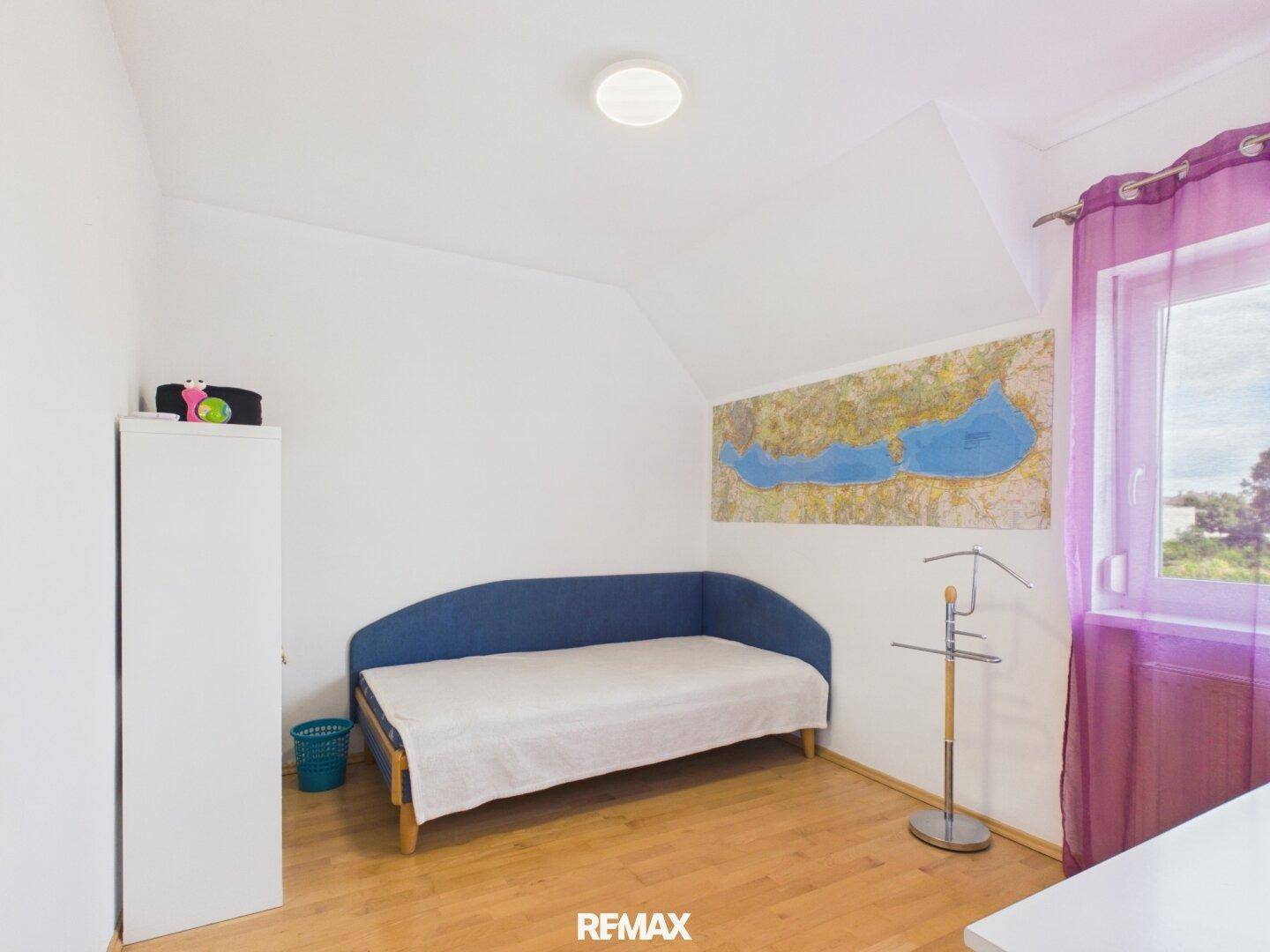 Helles Schlafzimmer mit Holzboden, Fenster und einem Einzelbett, einfach und funktional.
