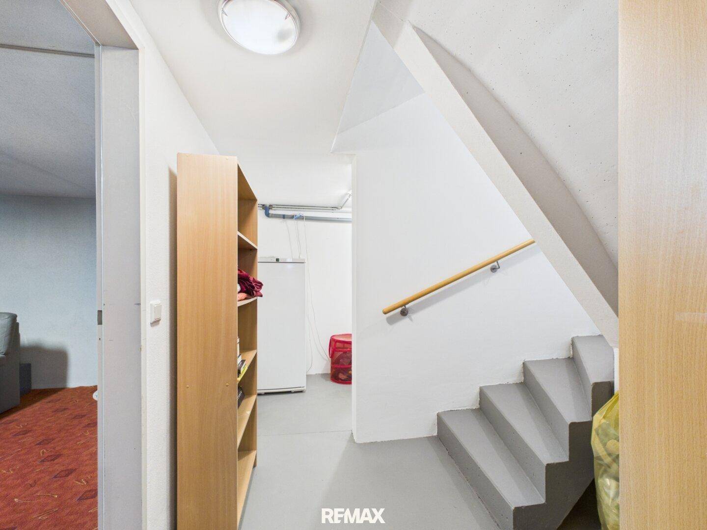 Kellerflur mit Treppenzugang, Regal und Kühlschrank, funktionaler Stauraum.