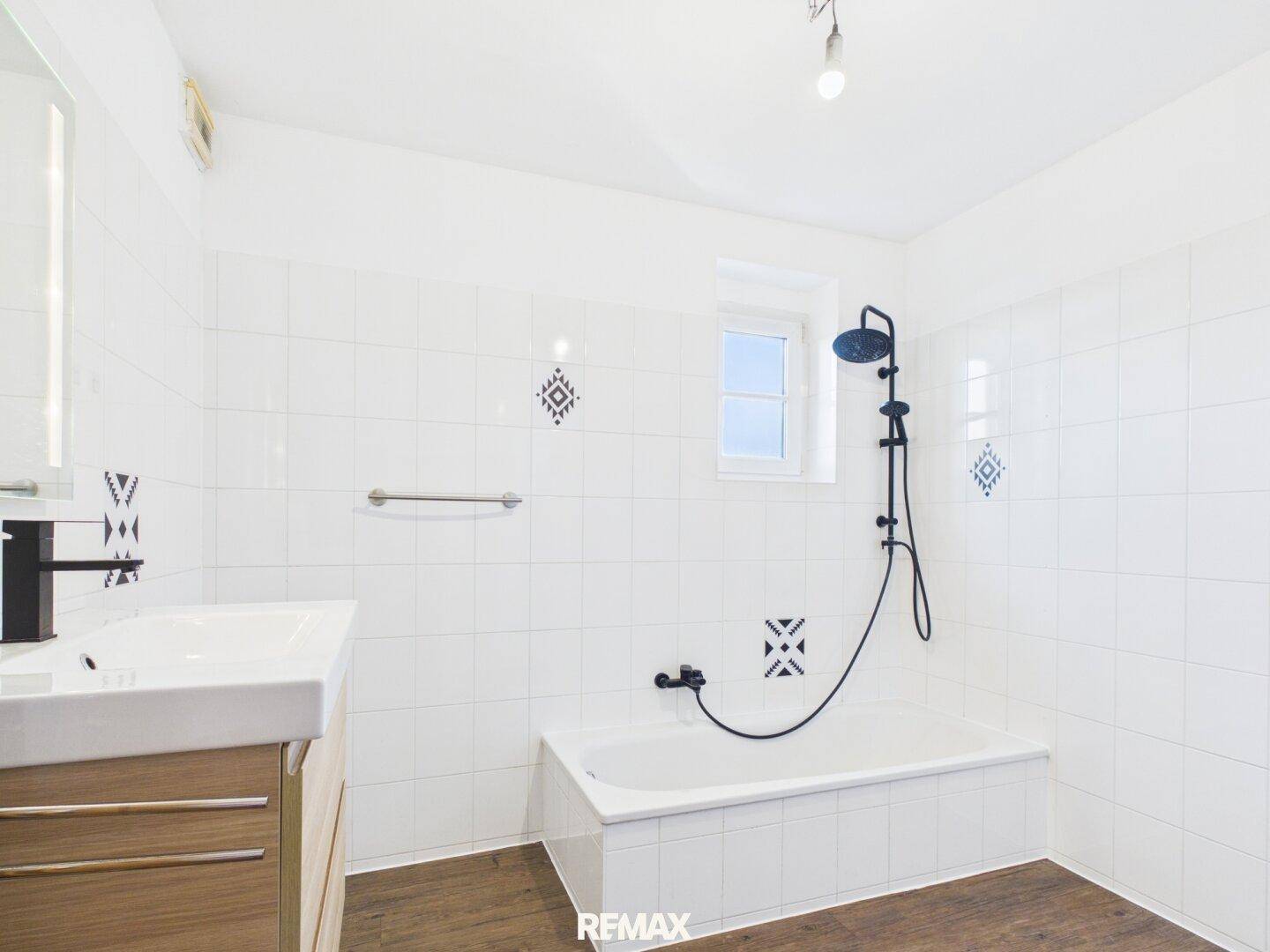 Modernes Badezimmer mit weißen Fliesen, Badewanne, Dusche und Fenster für Tageslicht.