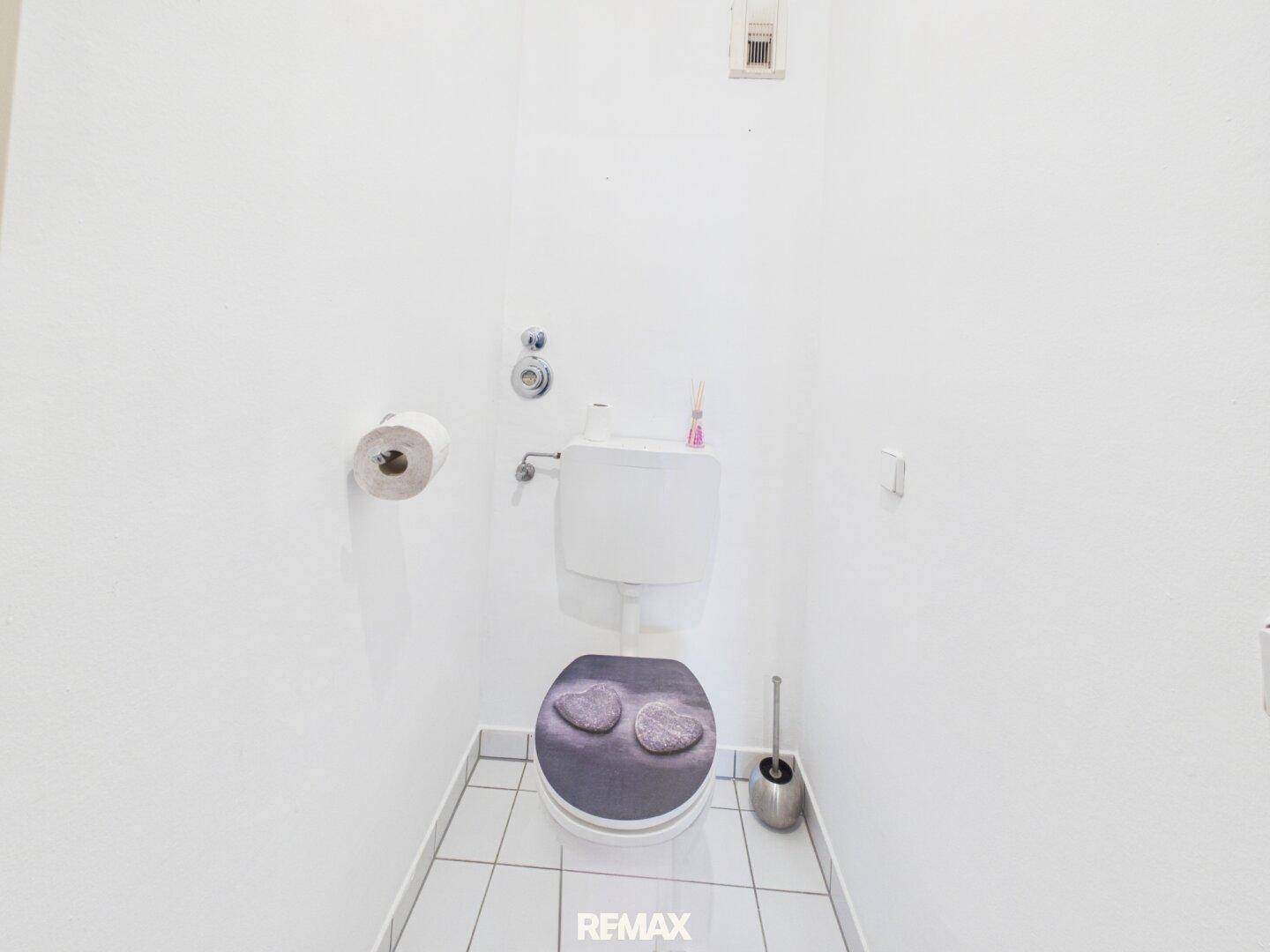 Separates WC mit weißer Toilette und hellen Fliesen, praktisch für Gäste.