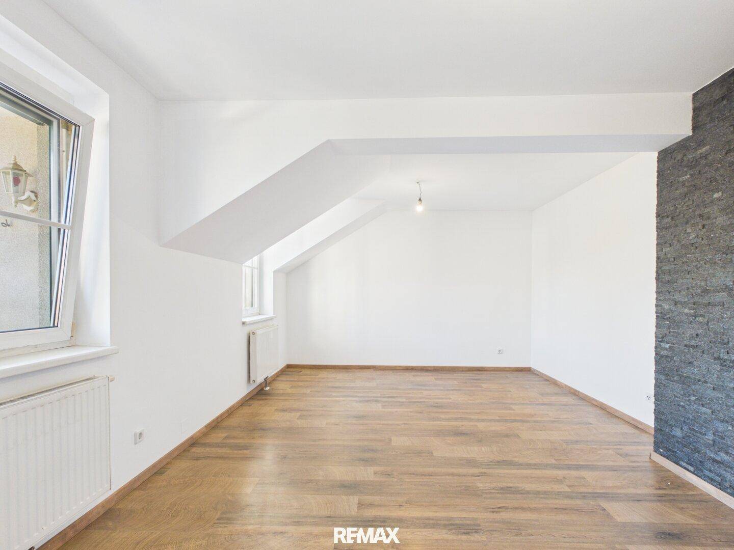 Geräumiges Wohnzimmer mit Holzboden, weißen Wänden und schräger Decke, bereit zur Einrichtung.