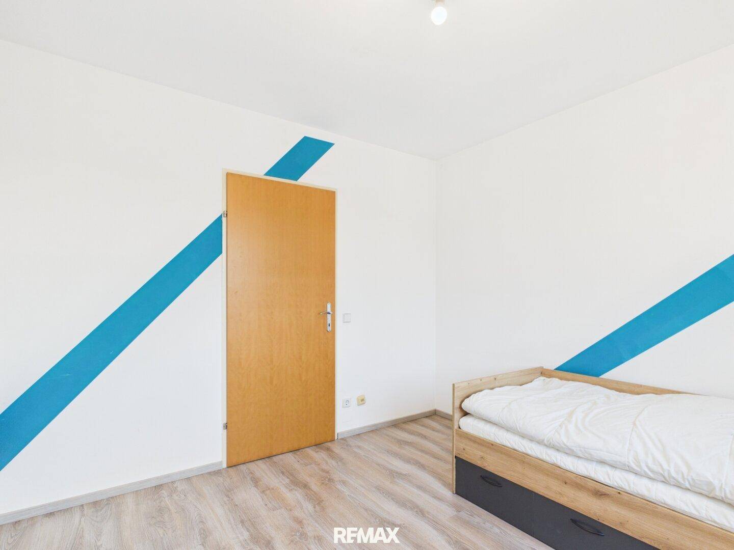 Schlafzimmer mit Holztür, Laminatboden und blauen Wandakzenten, bietet eine persönliche Note.