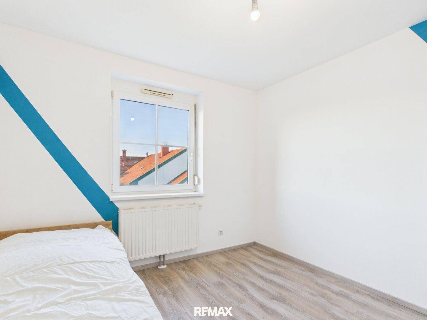 Schlafzimmer mit Einzelbett, Laminatboden und dekorativen blauen Streifen an der Wand.
