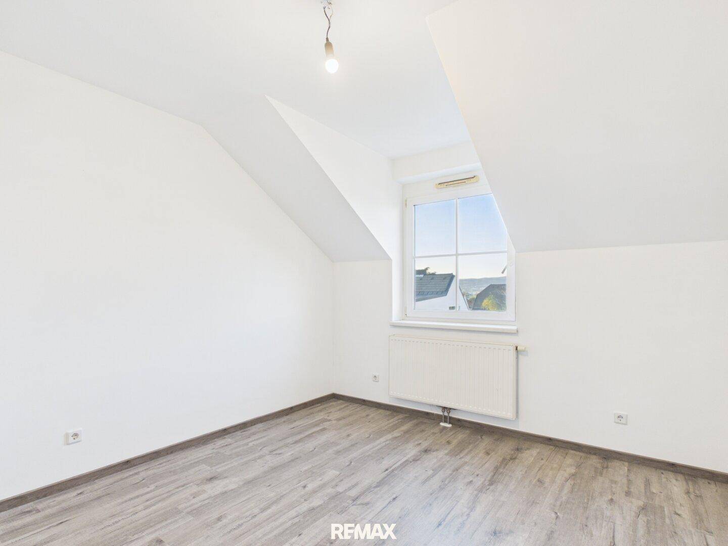 Helles Schlafzimmer mit Laminatboden, weißen Wänden und schräger Decke, unmöbliert.