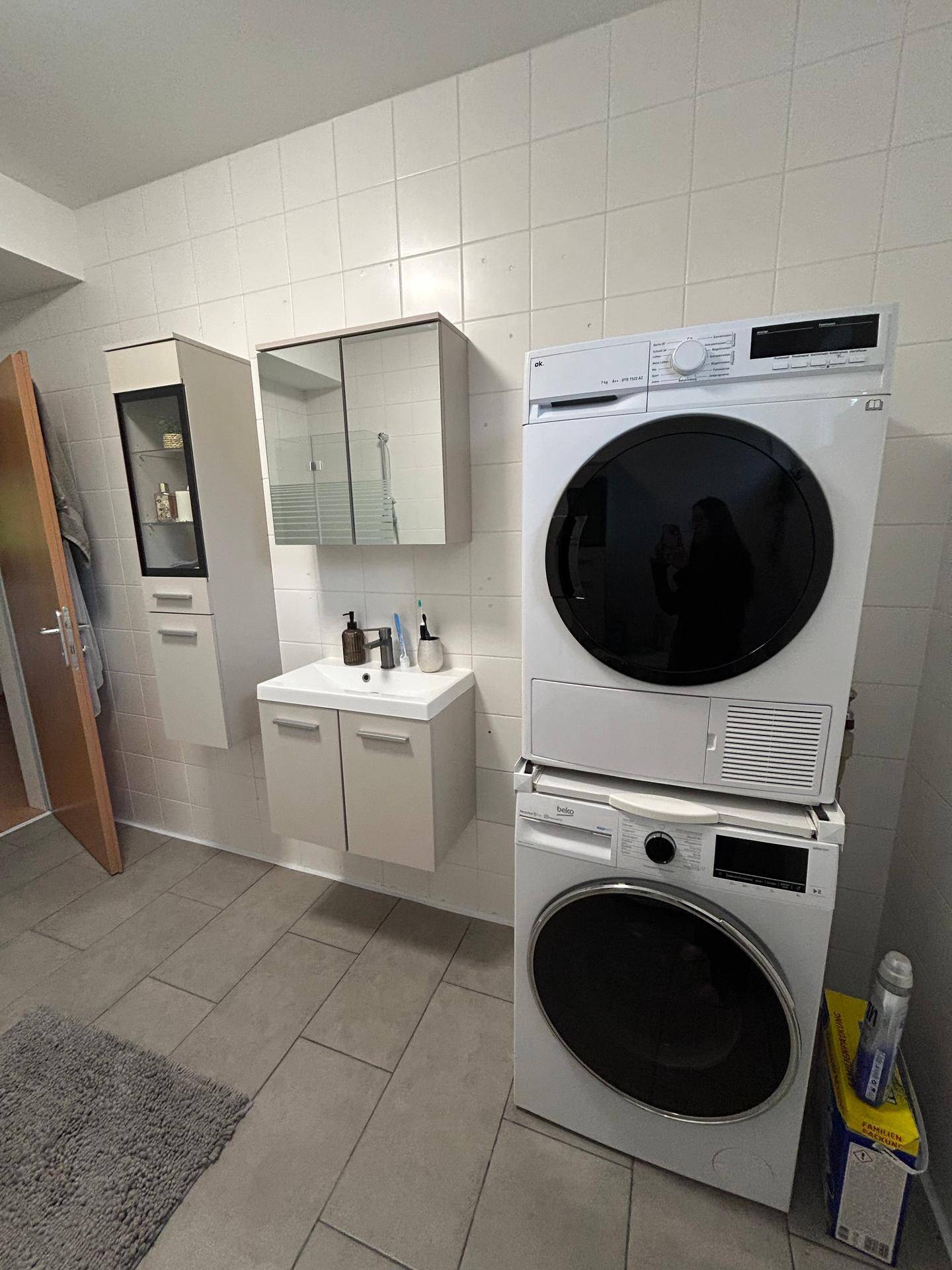 Funktionales Badezimmer mit Waschbecken, Spiegelschrank und integrierter Waschmaschine und Trockner.