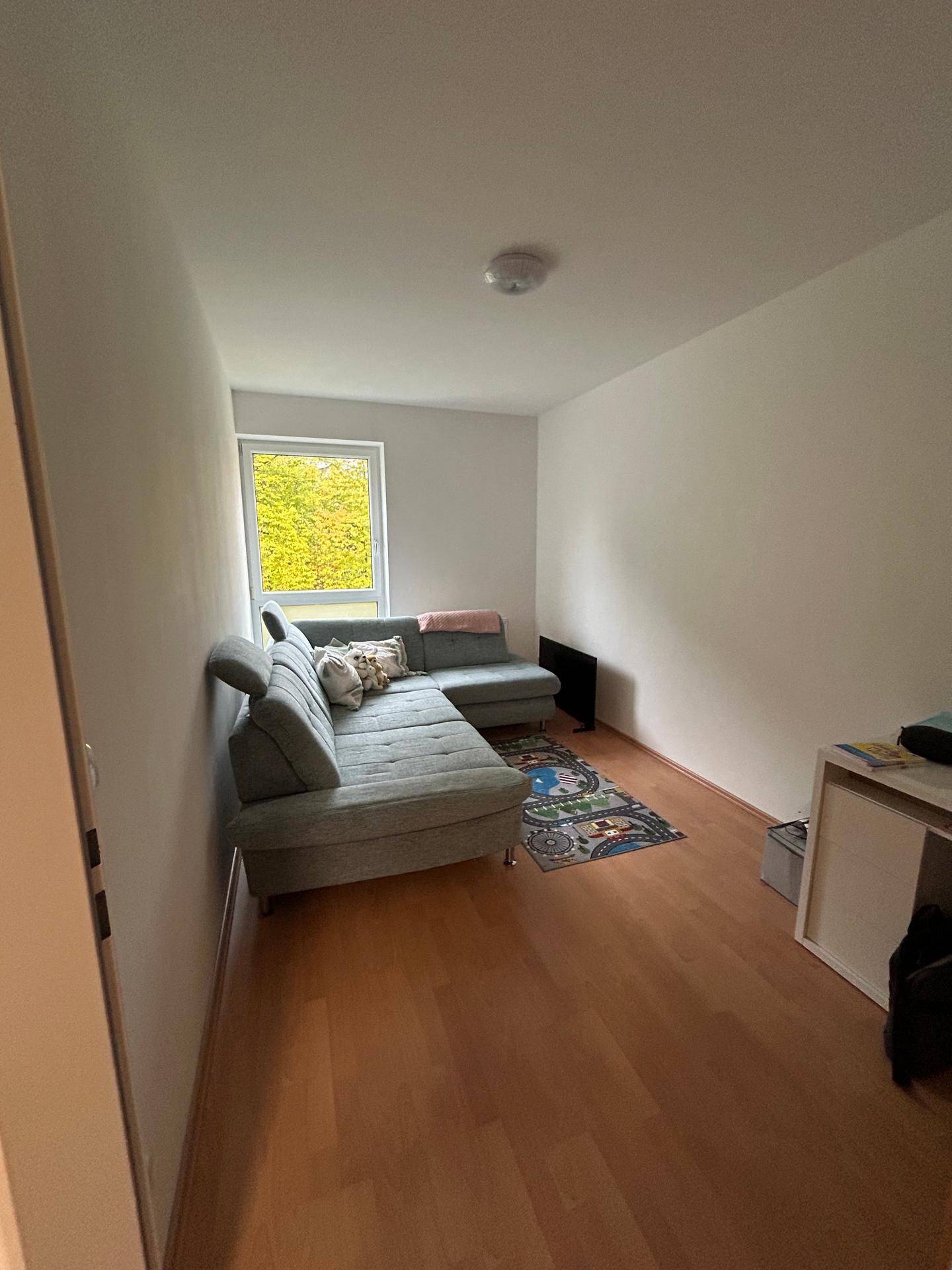 Helles Wohnzimmer mit Sofa, Holzboden und Fenster mit Blick ins Grüne.