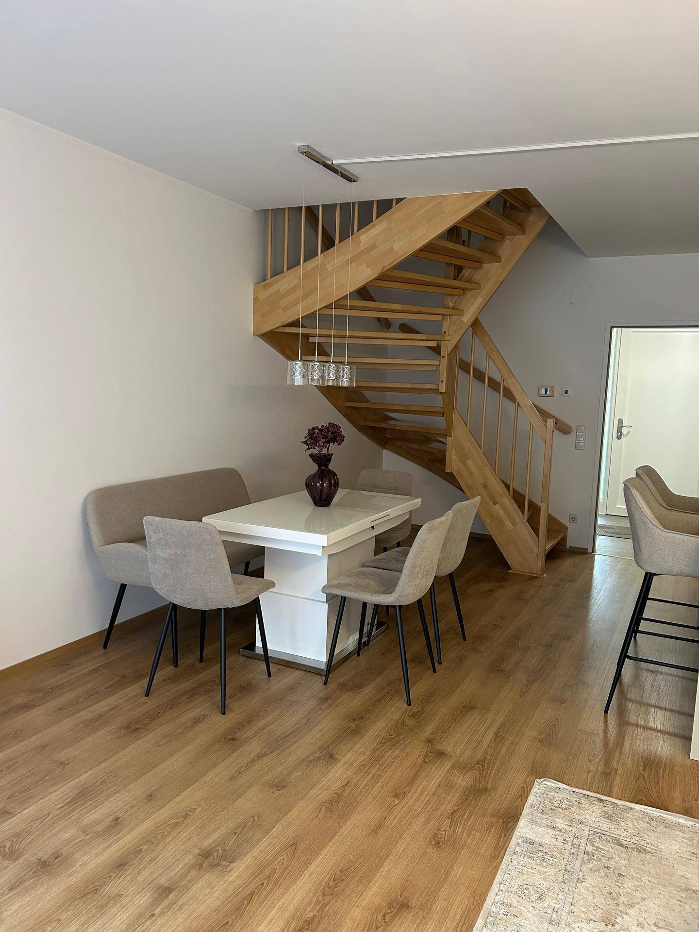 Heller Essbereich mit Holztisch, Stühlen und Holztreppe.