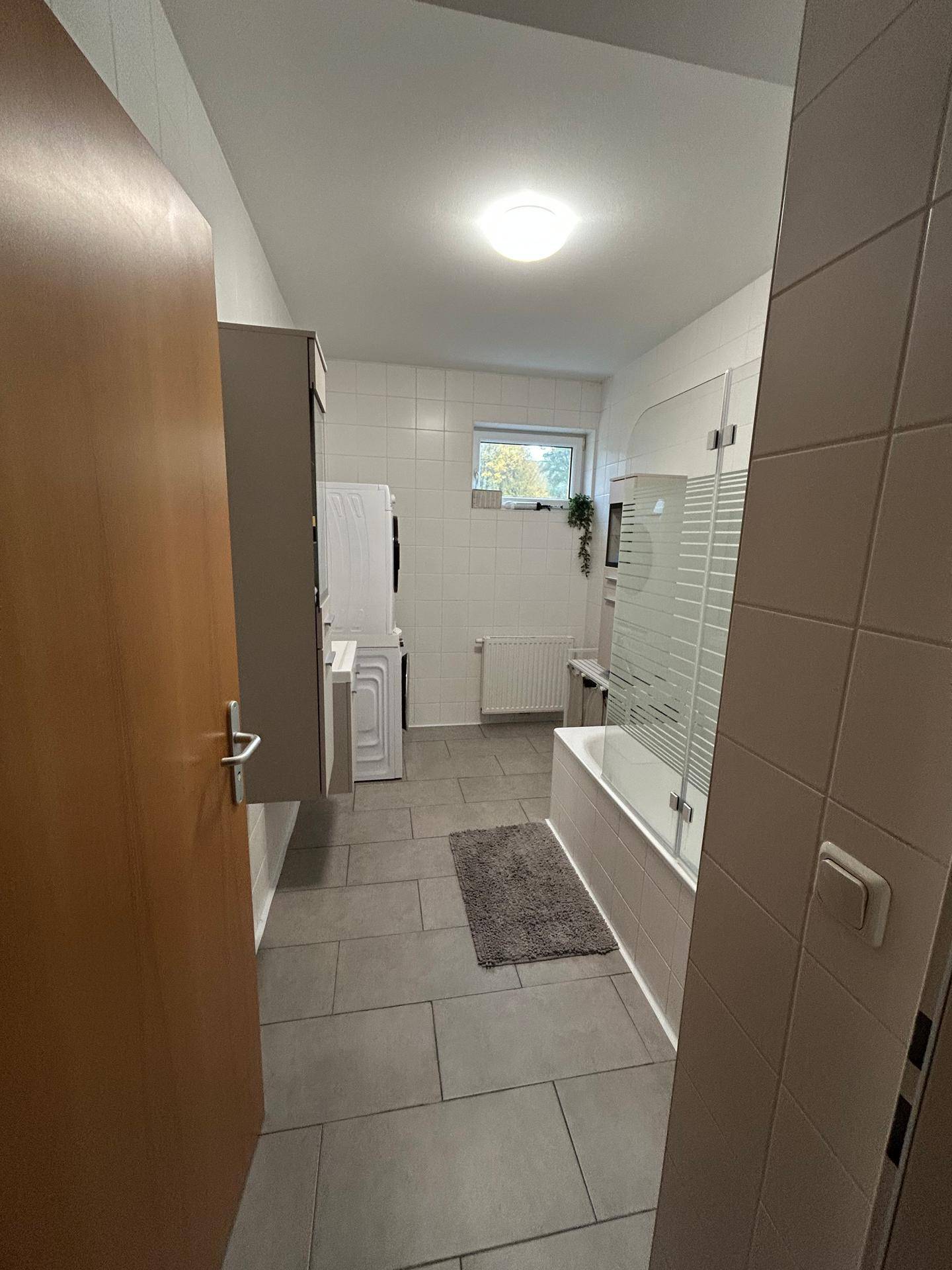 Badezimmer mit Badewanne, Fliesenboden und Fenster für Tageslicht.