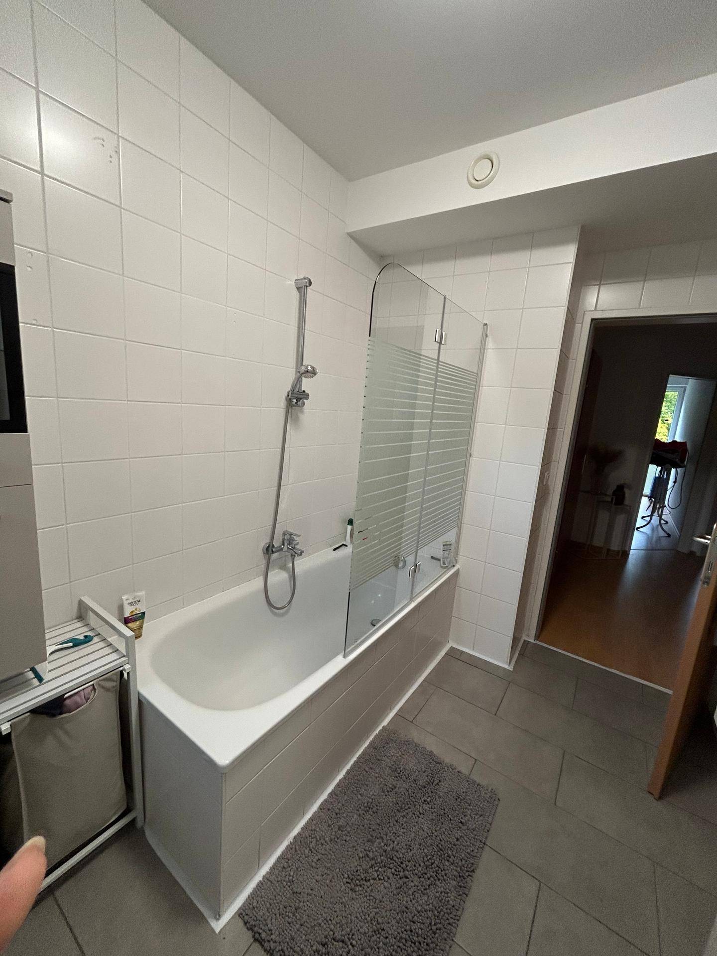 Badezimmer mit Badewanne inklusive Duschabtrennung und Fliesenboden.