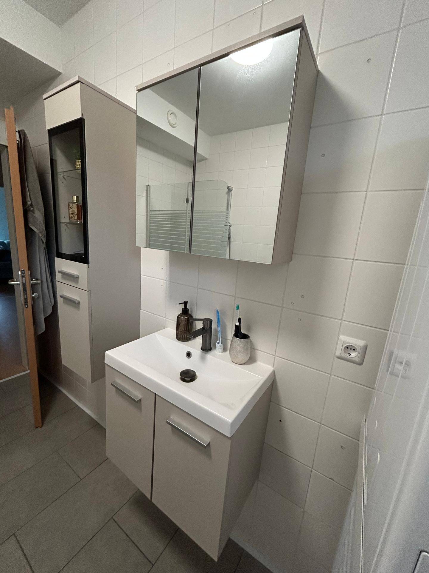 Modernes Badezimmer mit Einzelwaschbecken, Spiegelschrank und hellen Fliesen.