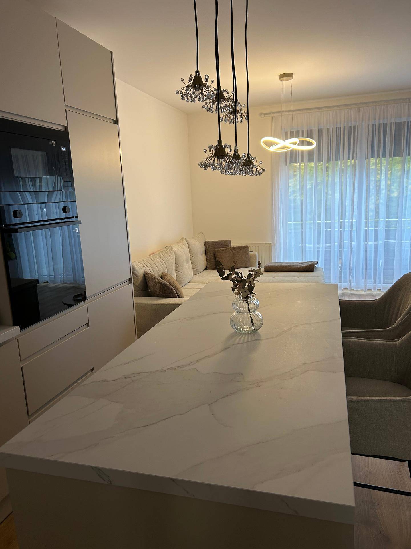 Offener Wohnbereich mit Kücheninsel, Sofa und großen Fenstern mit Vorhängen.