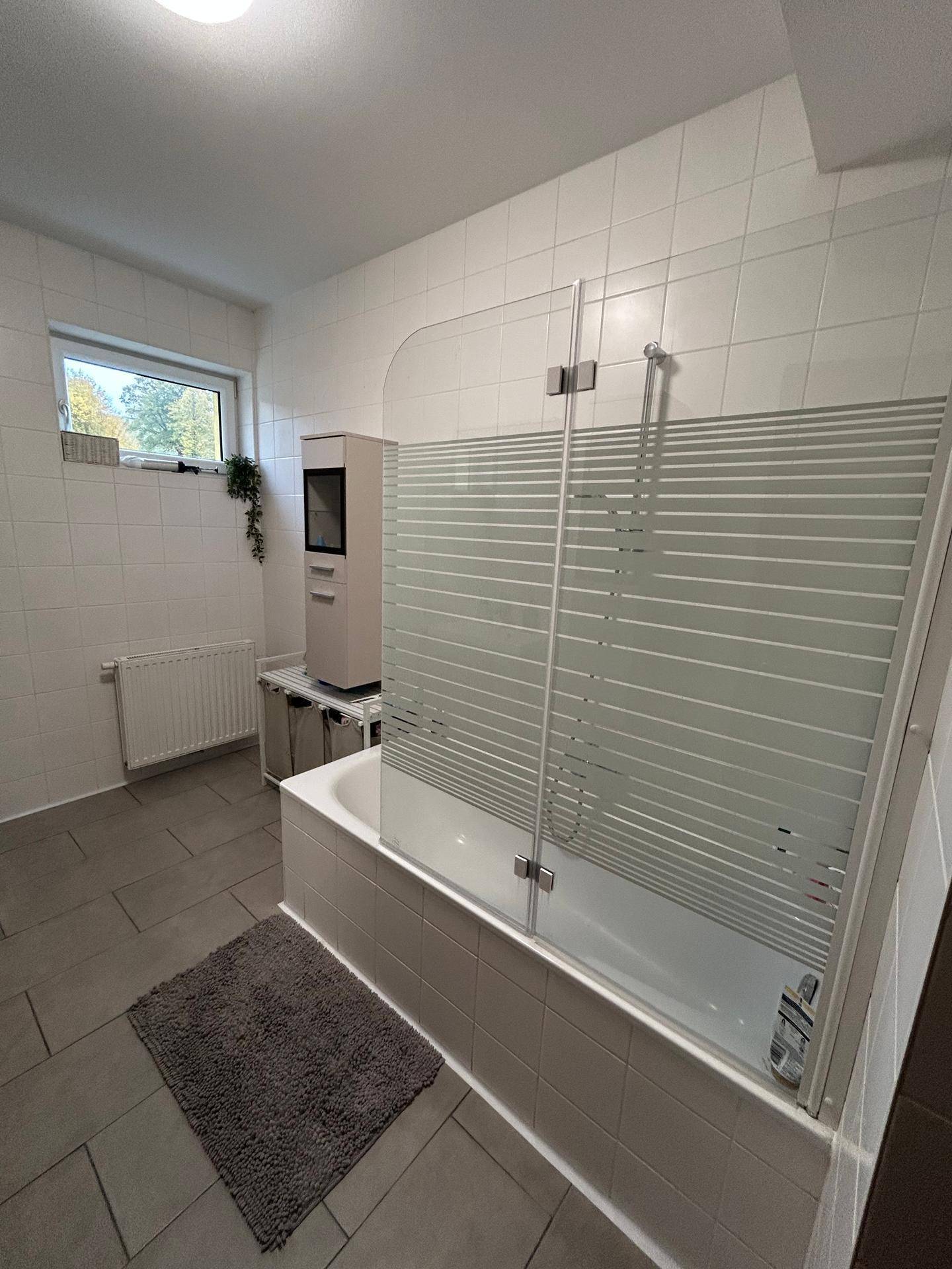 Badezimmer mit Badewanne, Duschabtrennung und Fenster für natürliche Belüftung.