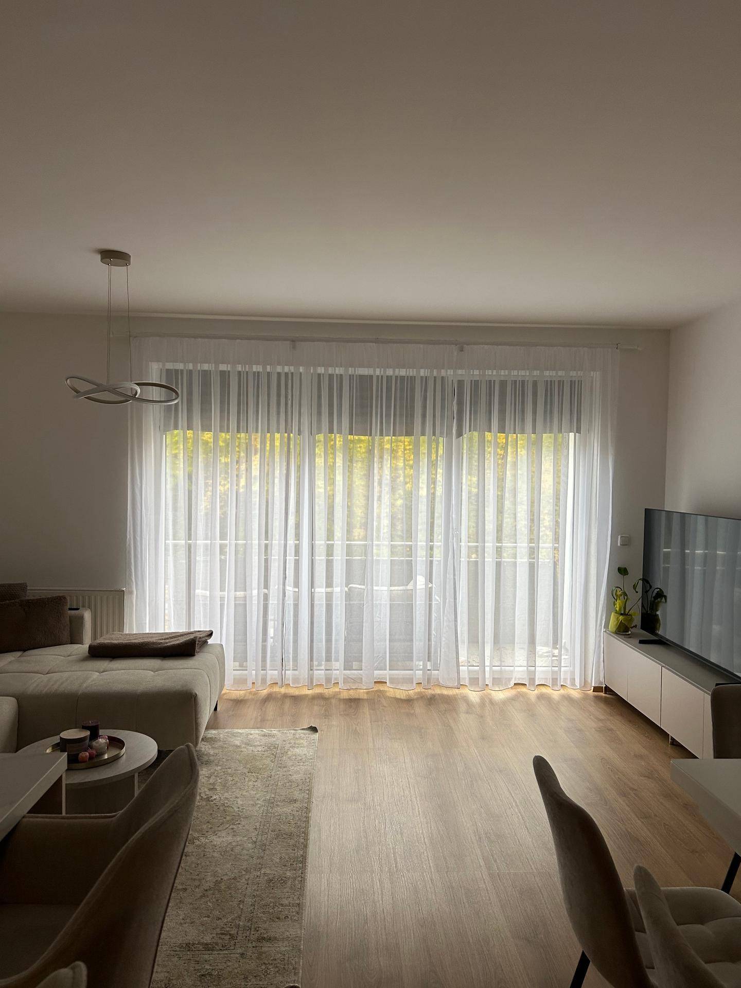 Lichtdurchflutetes Wohnzimmer mit großen Fenstern, Sofa und Holzboden.