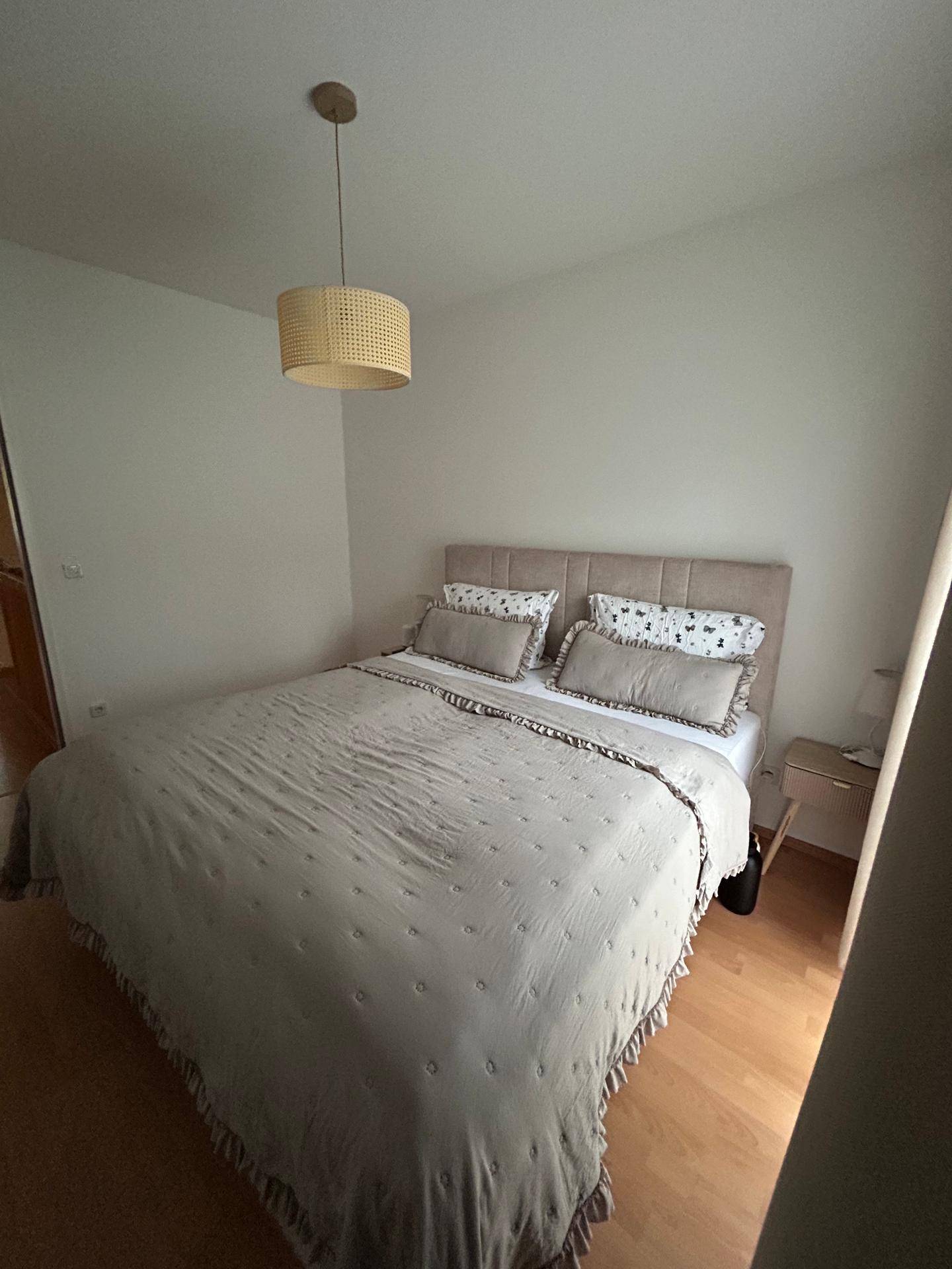 Helles Schlafzimmer mit großem Bett, Holzboden und schlichter Einrichtung.