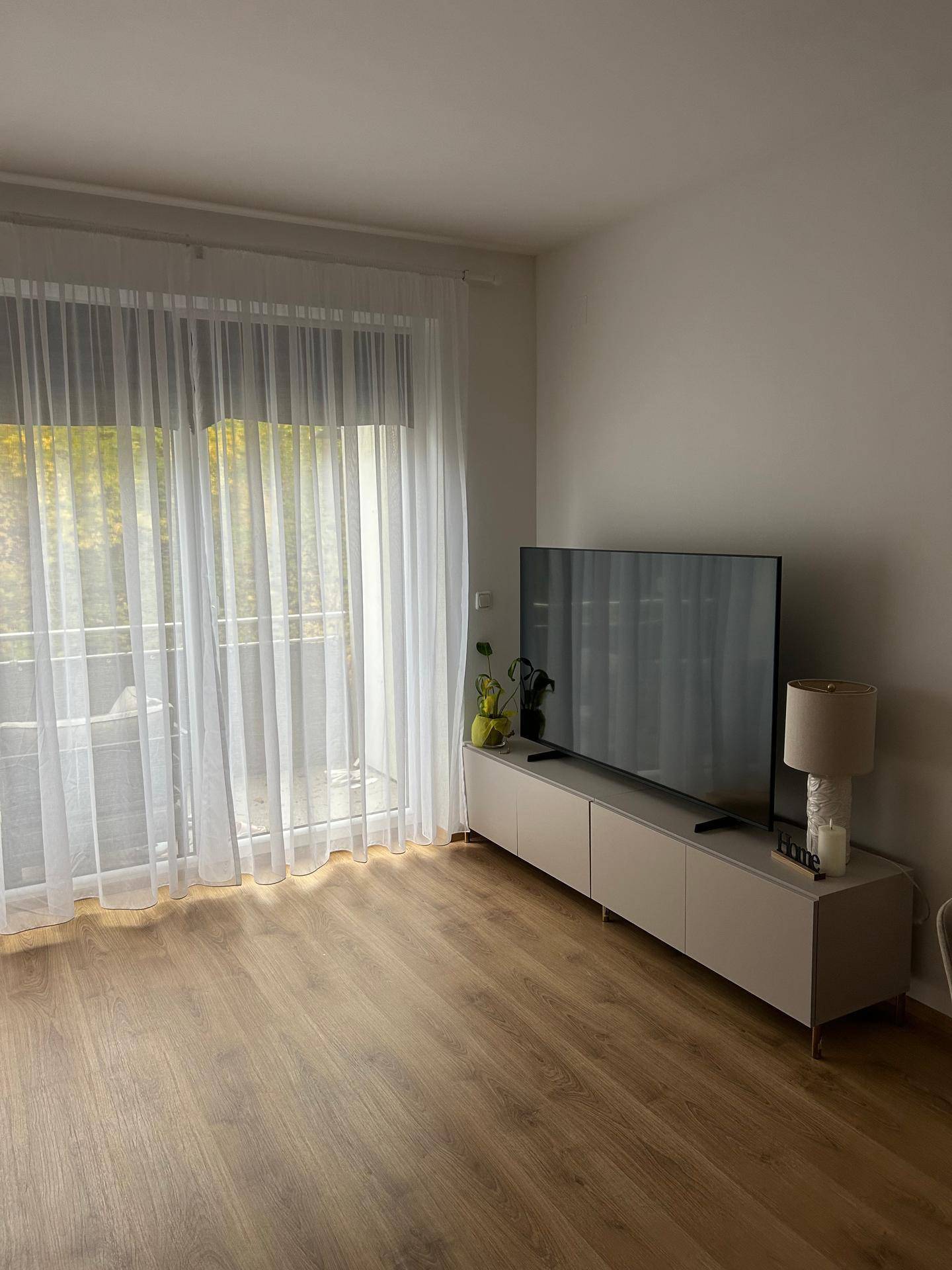 Helles Wohnzimmer mit modernem TV-Möbel, Laminatboden und direktem Zugang zum Balkon.