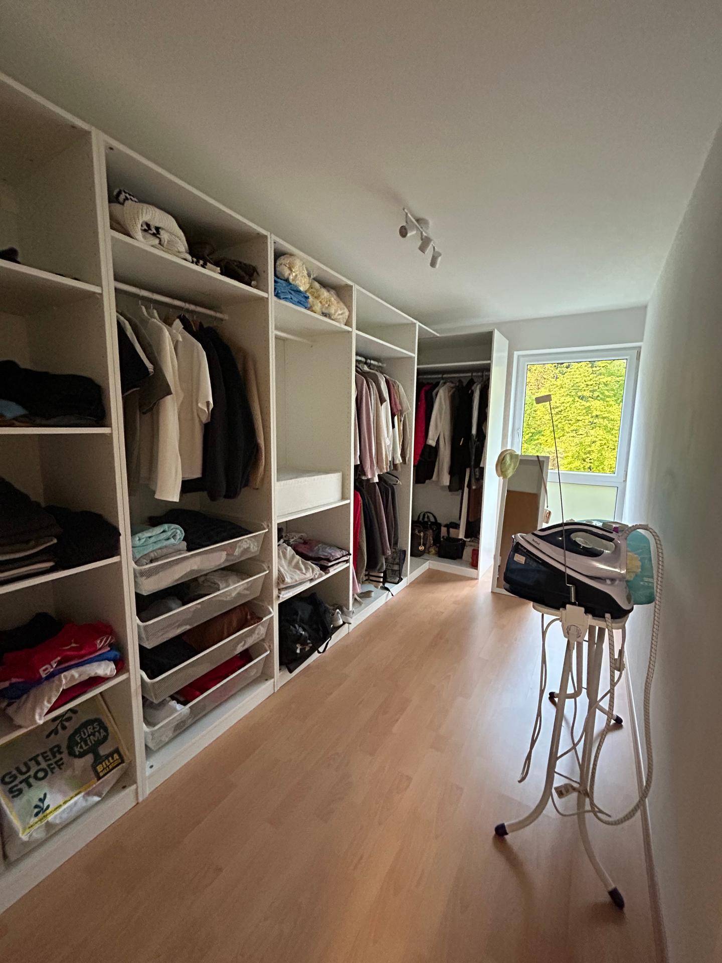 Begehbarer Kleiderschrank mit offenen Regalen und Fenster für Tageslicht.
