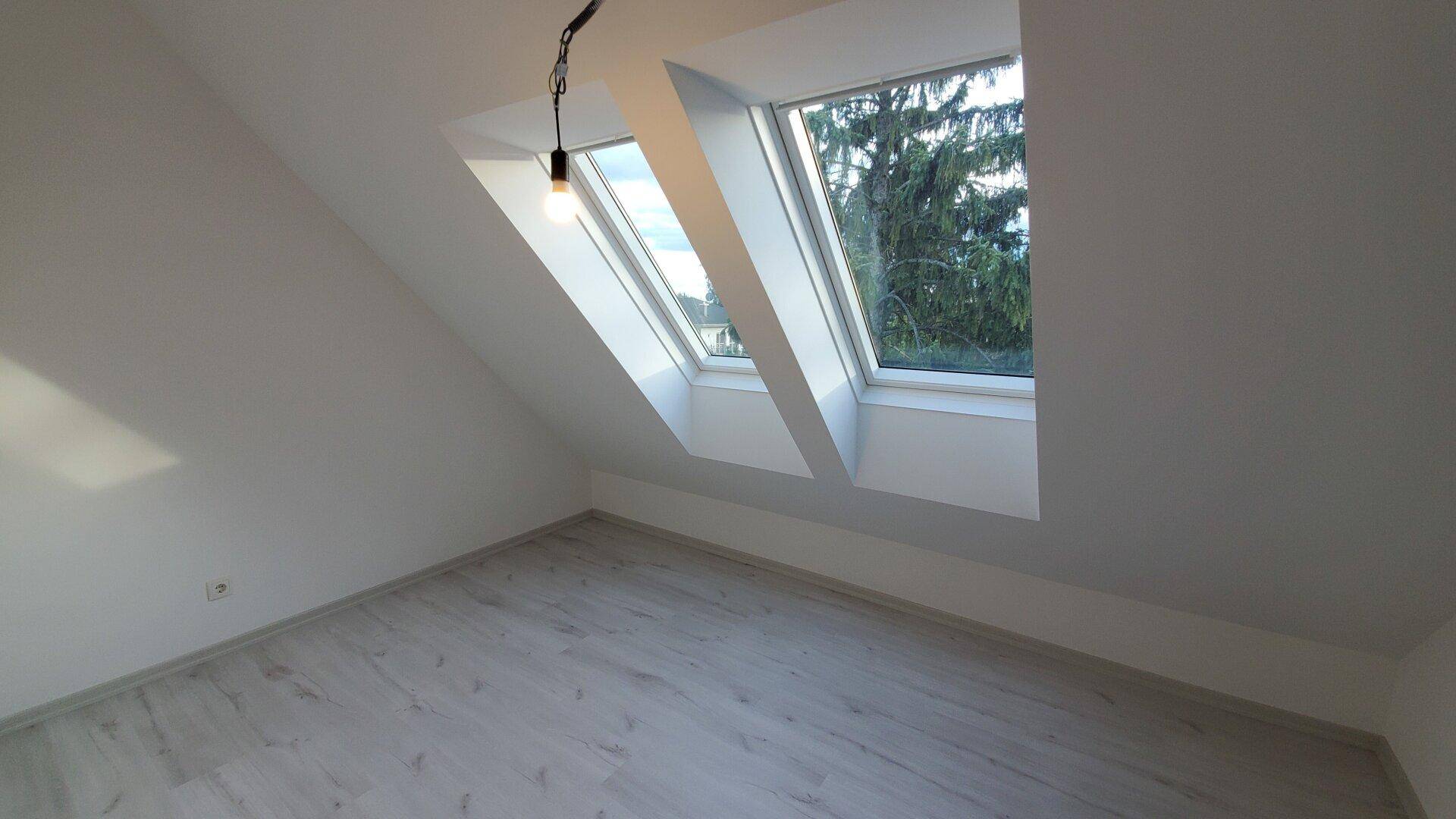 Heller Raum mit Dachschräge und zwei Dachfenstern, ausgestattet mit hellem Laminatboden.