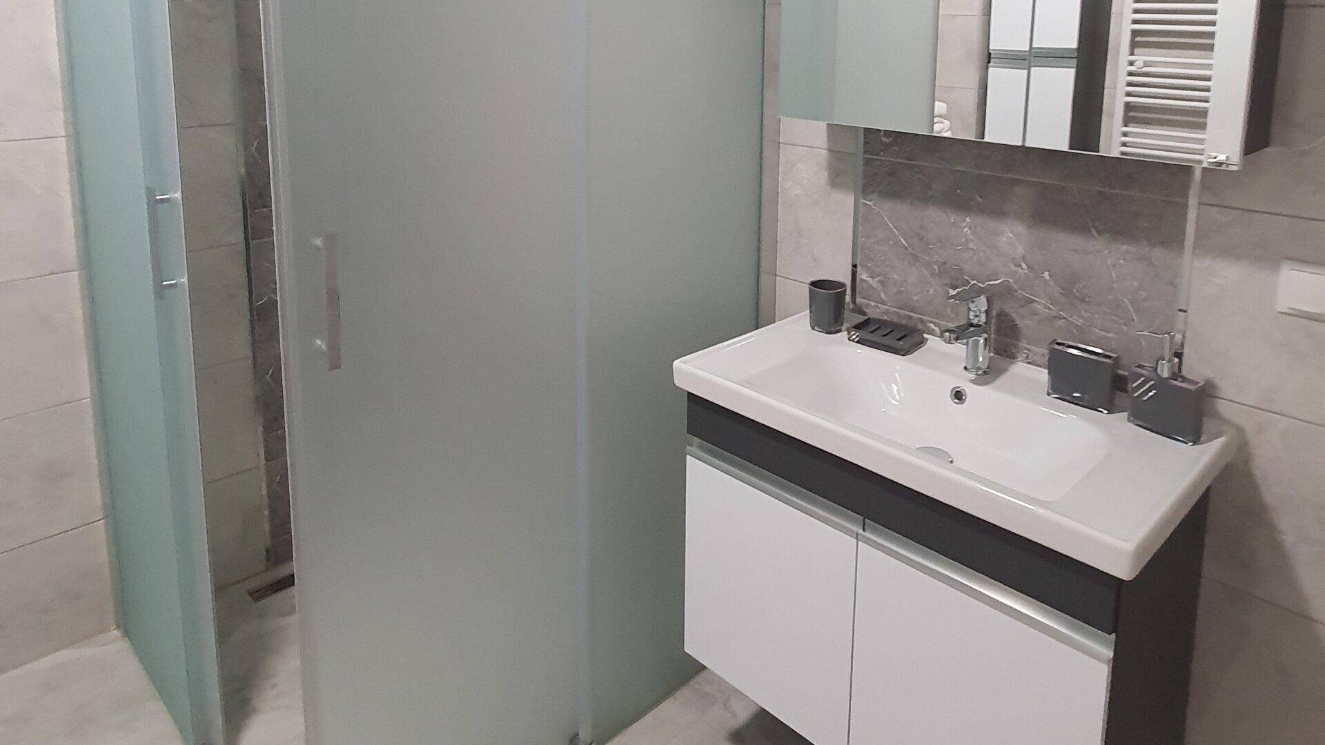 Modernes Badezimmer mit Duschkabine, Einzelwaschbecken und Spiegelschrank, gefliest in Grautönen.