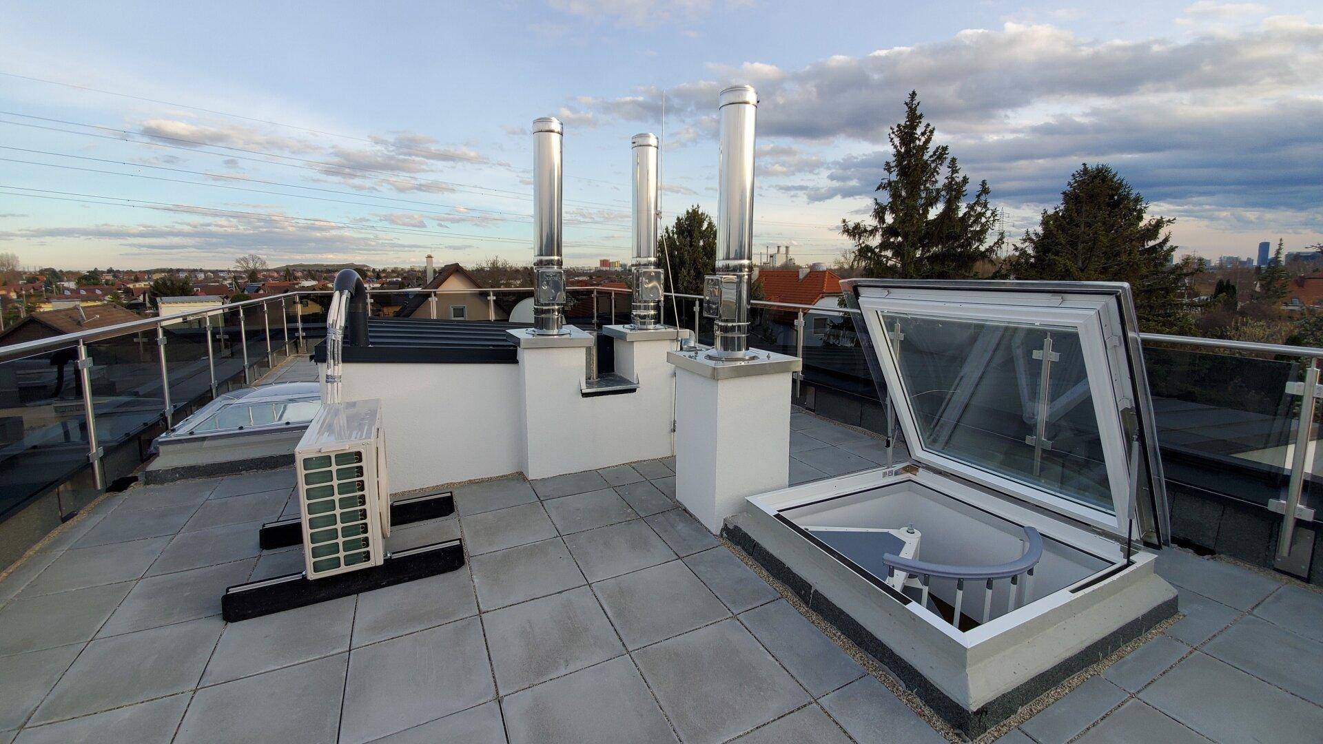 Geräumige Dachterrasse mit Fliesenboden, Glasgeländer und Blick über die Umgebung.