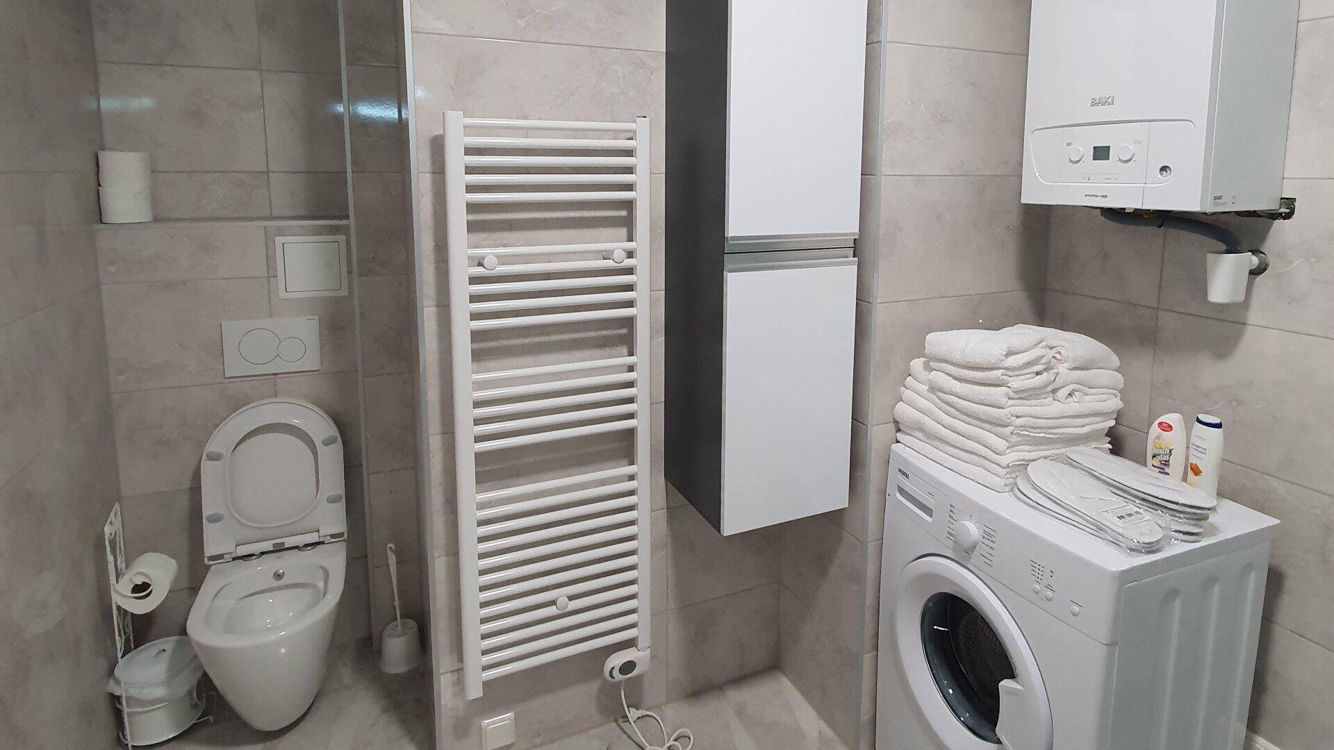 Funktionales Badezimmer mit WC, Waschmaschine, Handtuchheizkörper und Wandheizkessel.