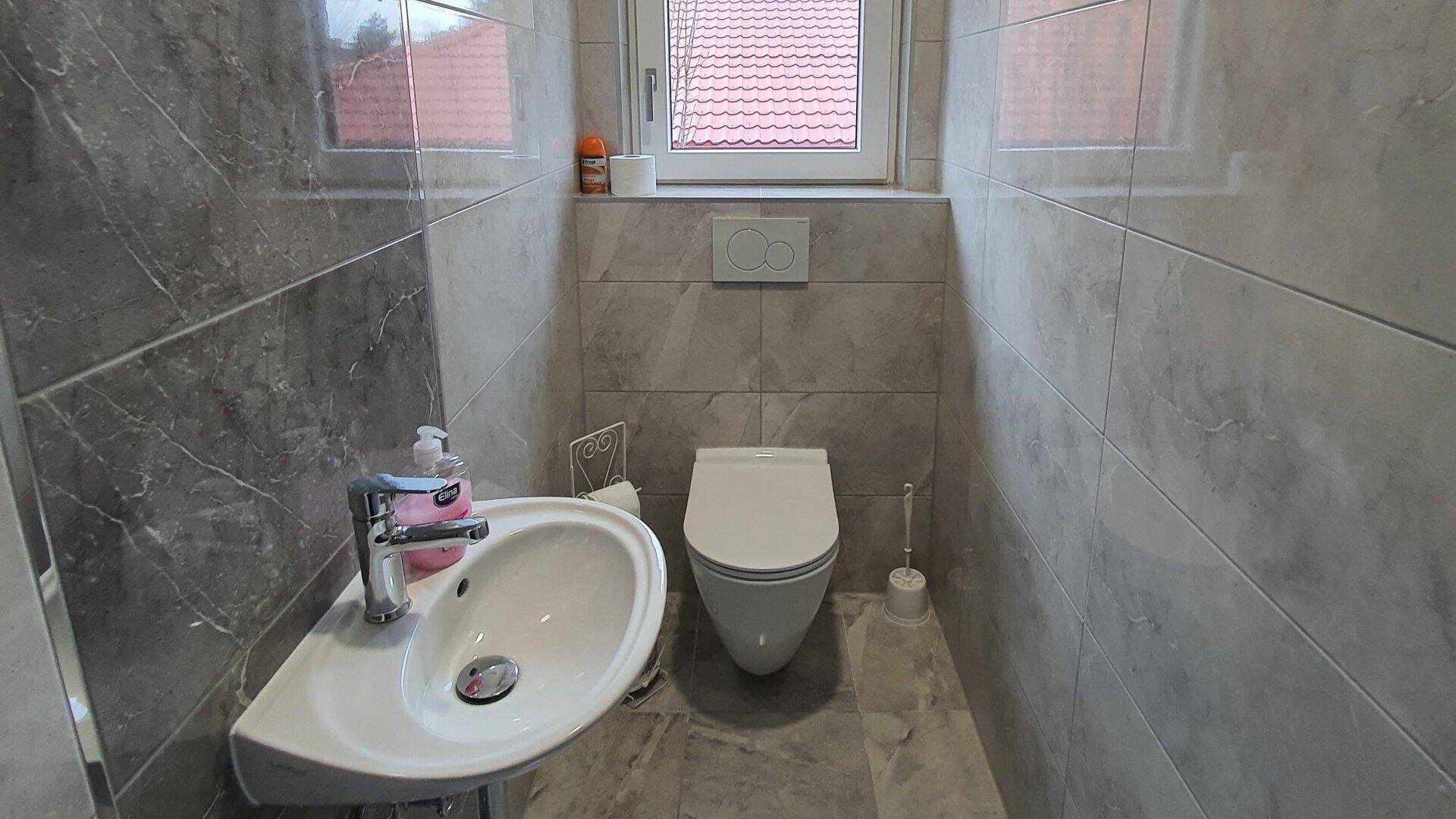 Kleines Gäste-WC mit Wand-WC, modern gefliesten Wänden und Fenster für Tageslicht.