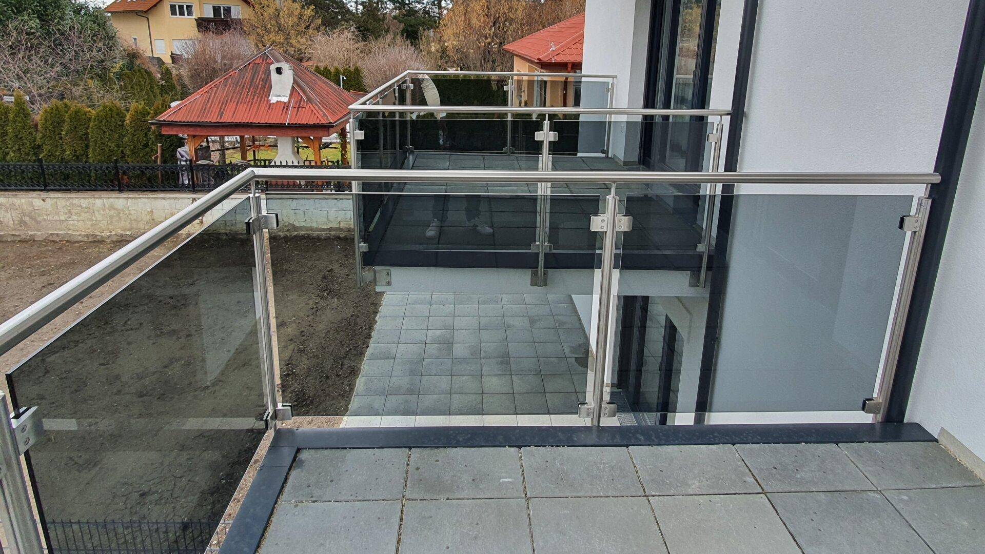 Moderner Balkon mit Glasgeländer und Blick auf die umliegenden Häuser und Gärten.