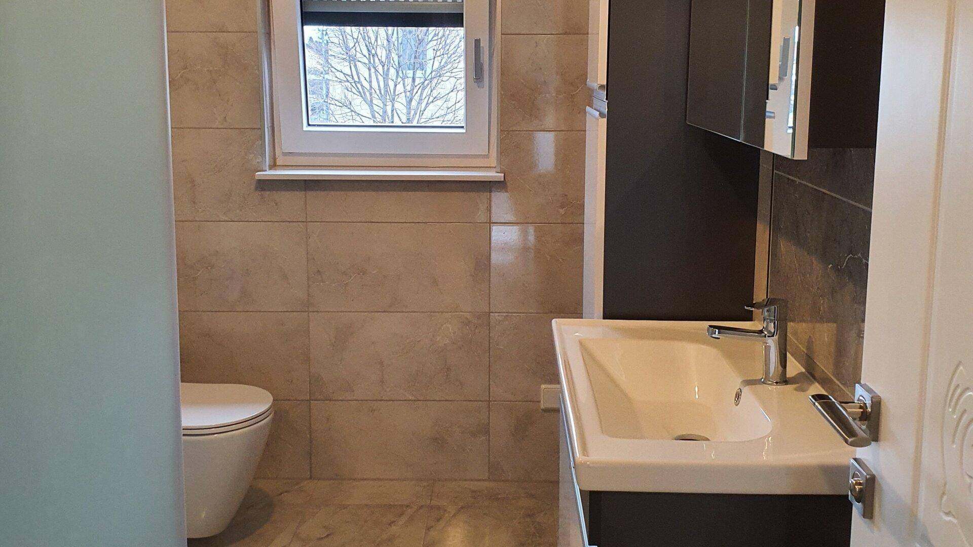 Badezimmer mit WC, Waschtisch und Fenster, das für natürliche Belüftung sorgt.